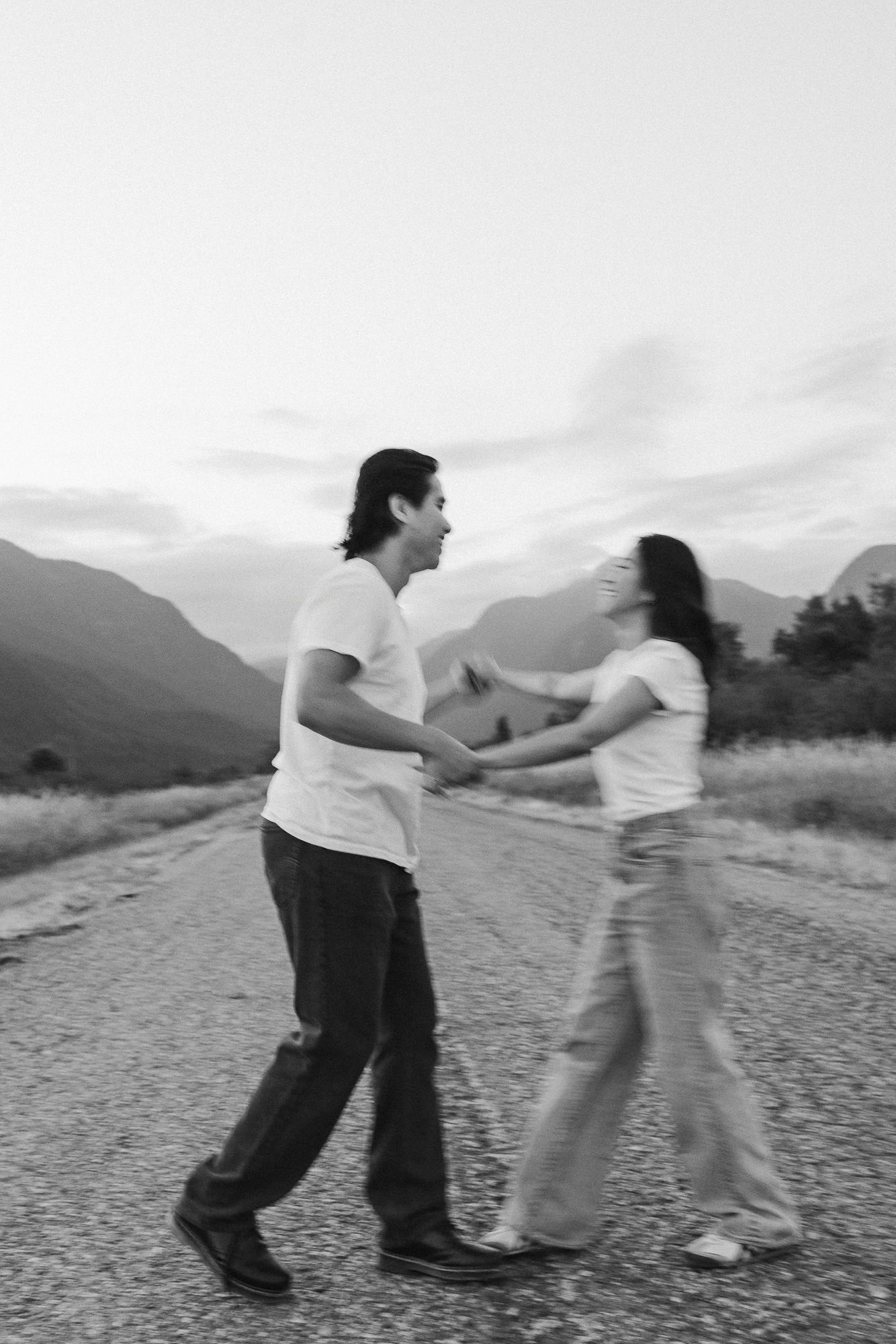 Black and white motion-blurred photo of a couple dancing hand in hand on a rural mountain road.