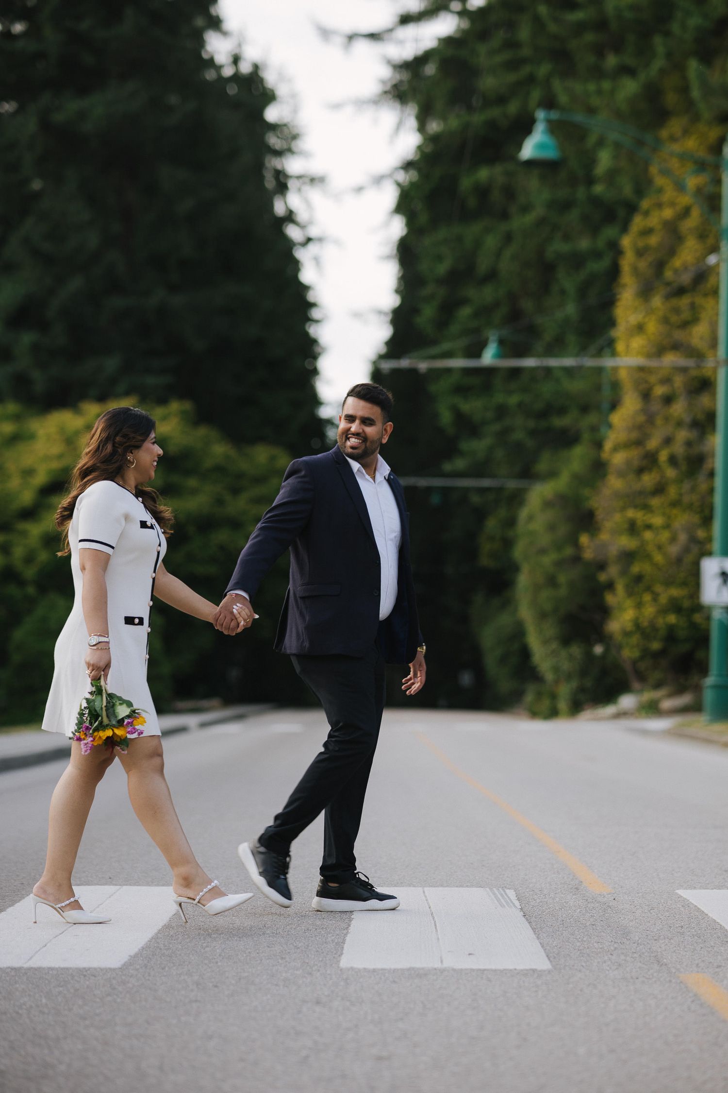 A couple recreates the iconic Abbey Road Beatles album cover pose on an empty road with trees in the background.
