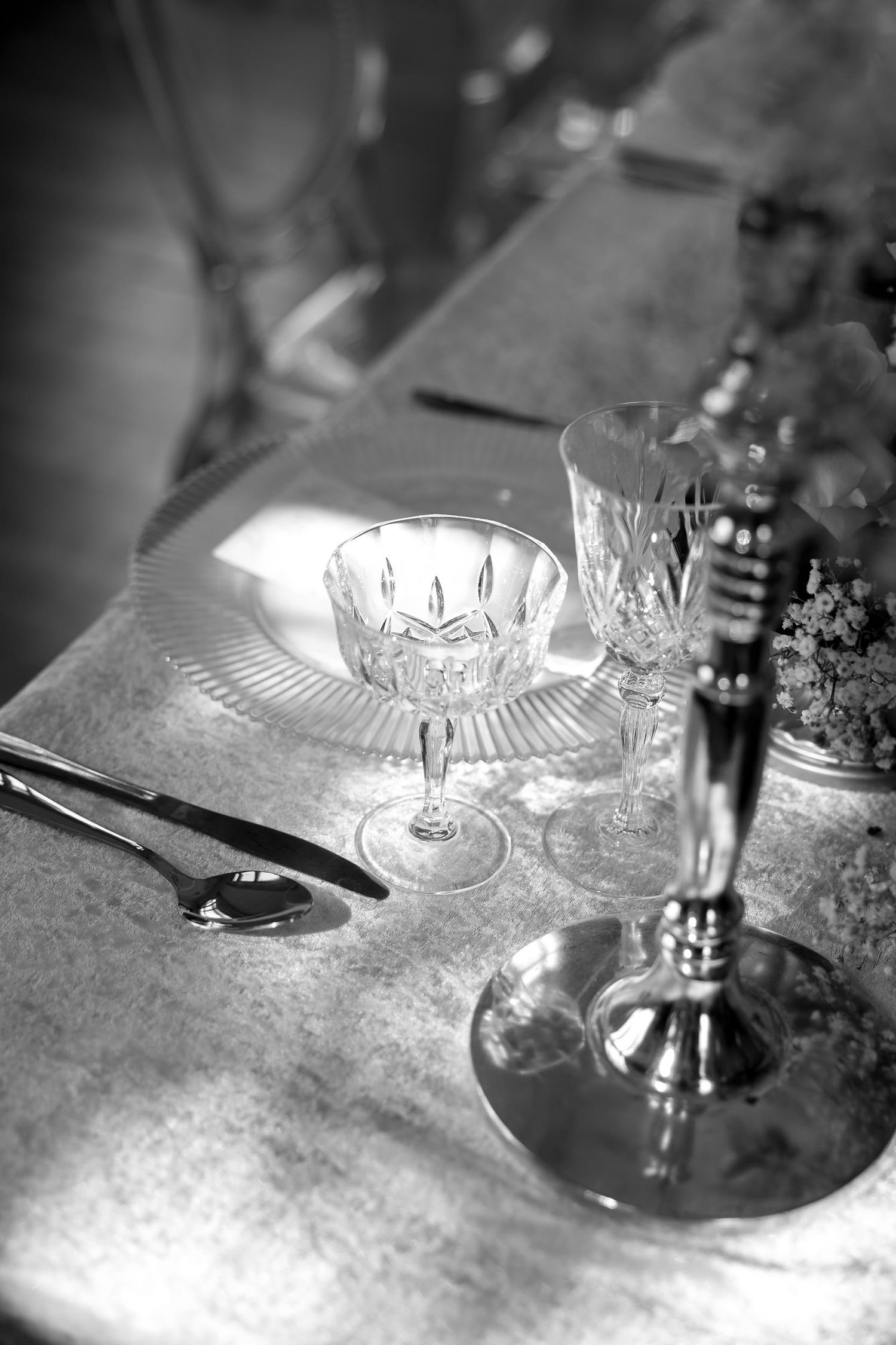 Crystal wine glasses and silver candlesticks arranged on an elegant table setting in black and white.