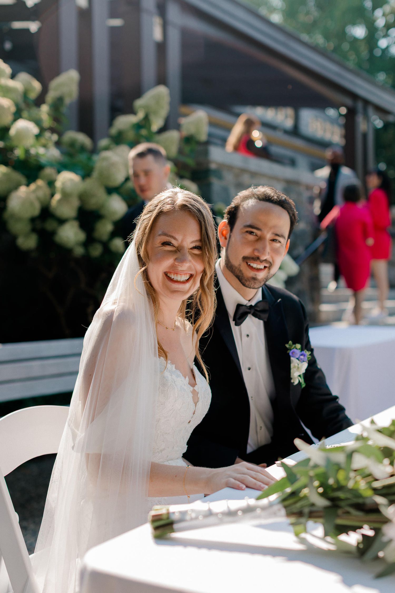 A happy couple shares joyful moments at their elegant outdoor wedding celebration with white floral decorations.