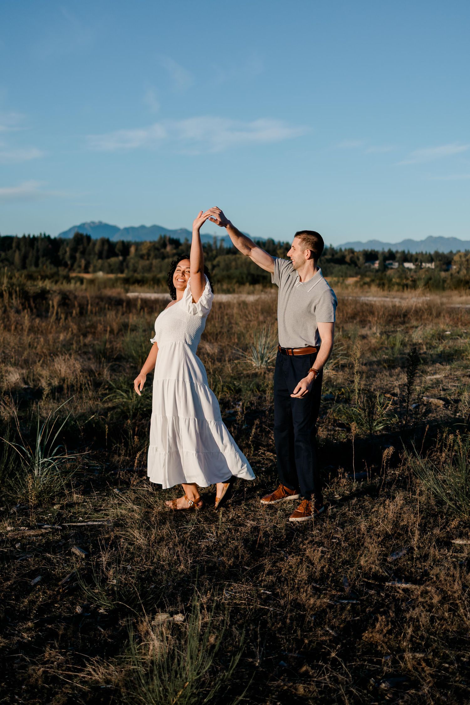 A couple dances together in a desert landscape with mountains in the background during golden hour.