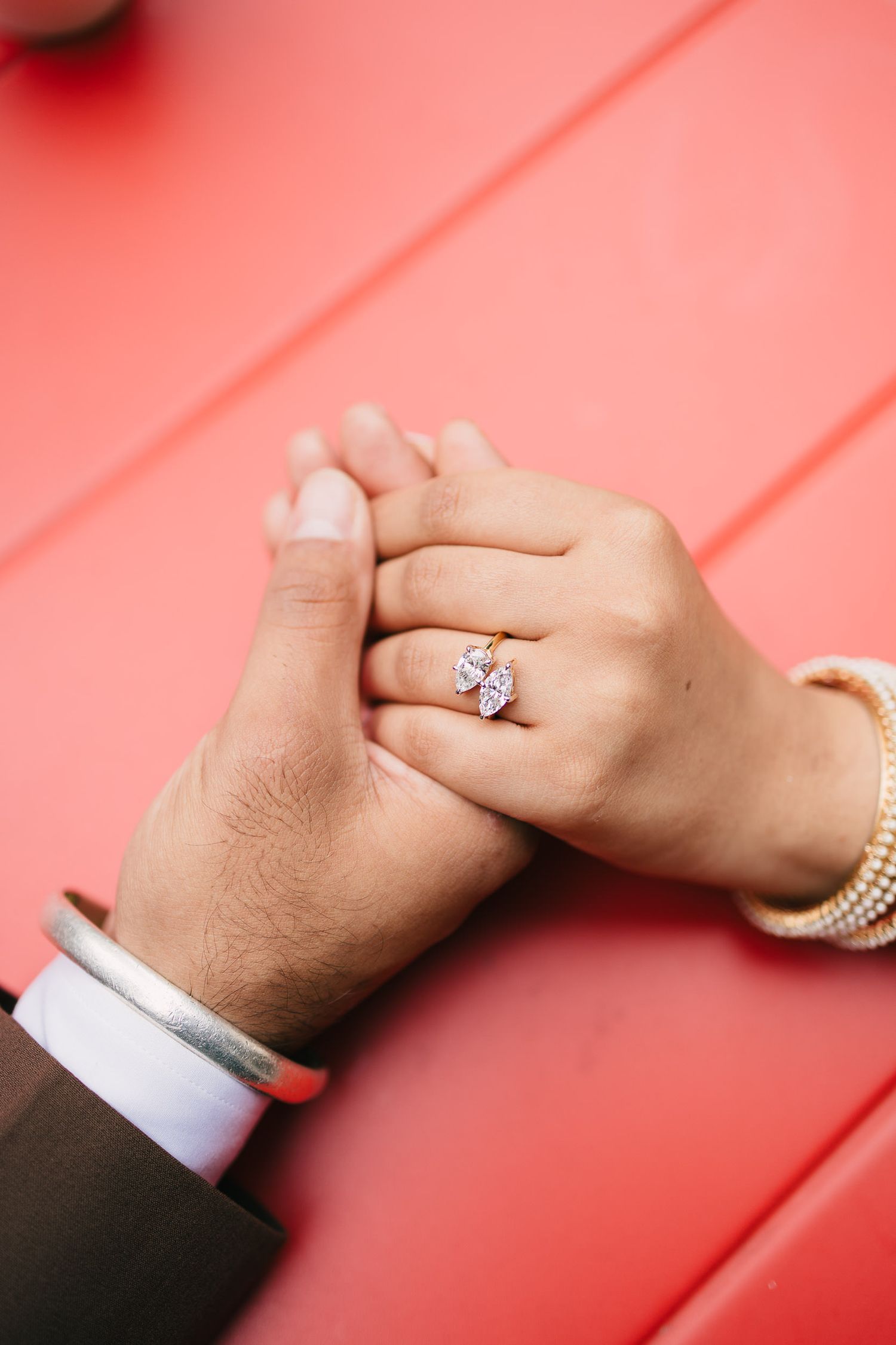 Two hands intertwined with an engagement ring against a coral-colored background in a series of romantic poses.