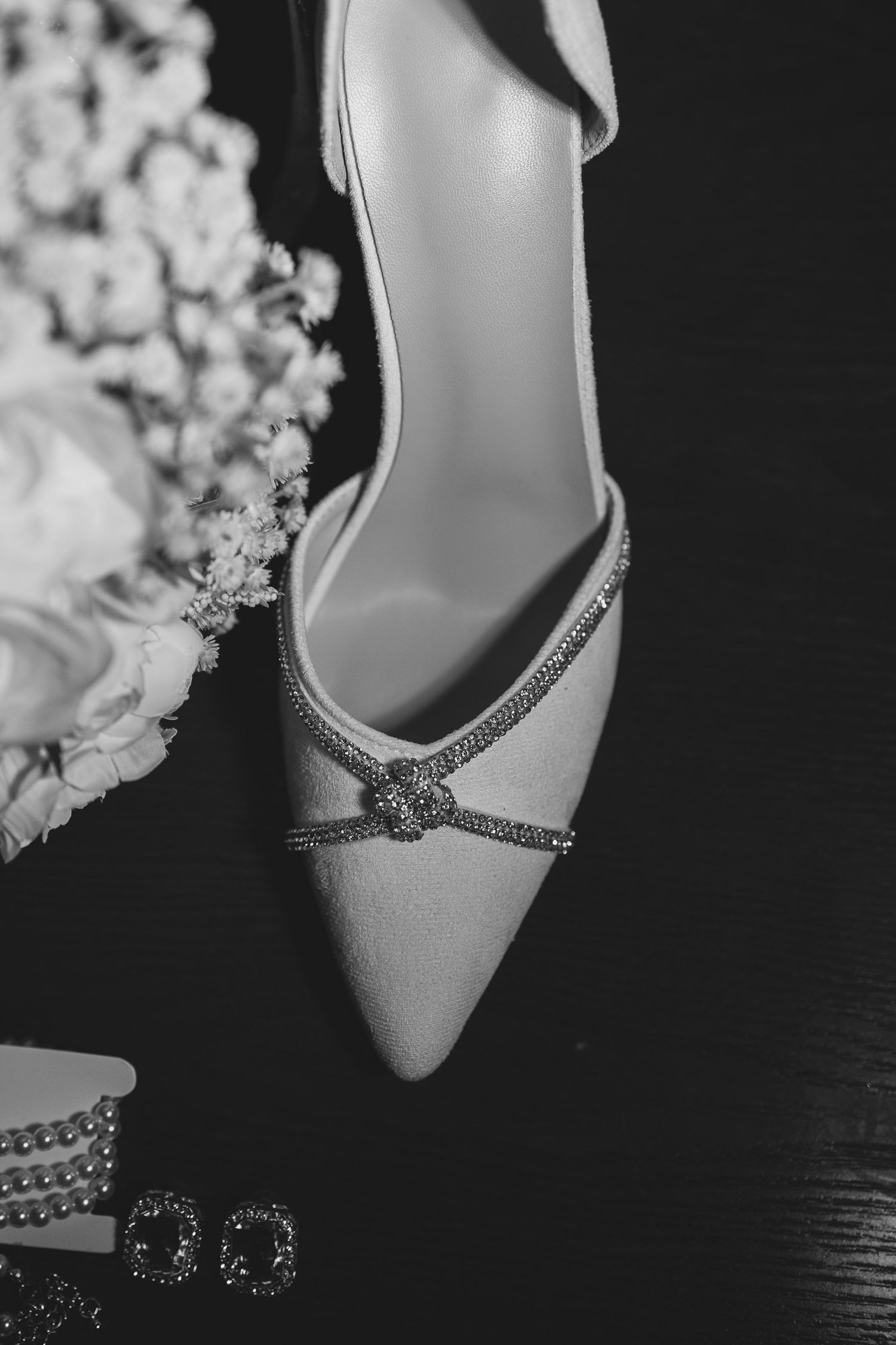 Elegant white bridal heels with sparkling crystal embellishments displayed alongside delicate white flowers.