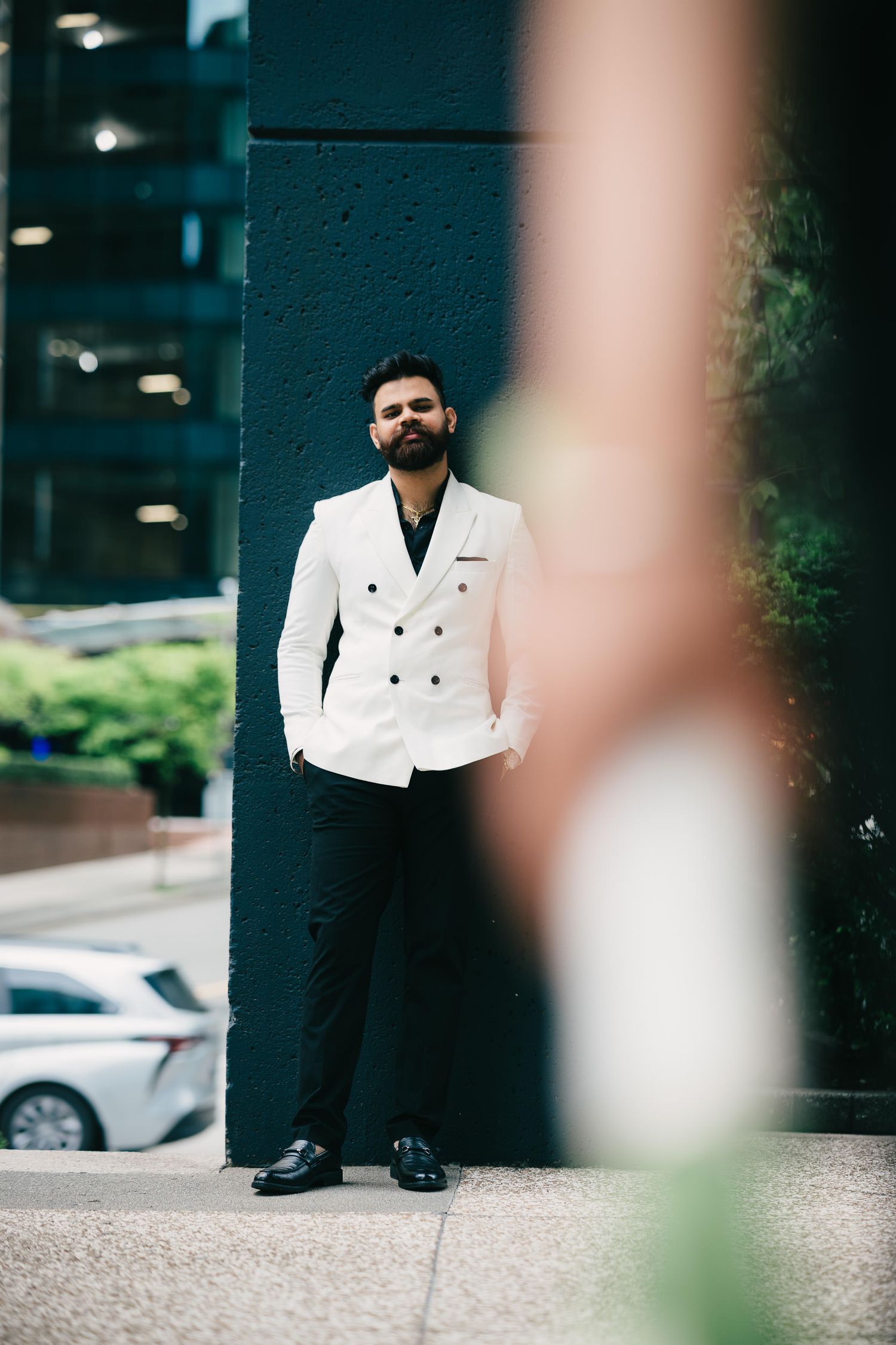 Person in a crisp white double-breasted blazer and black pants stands outside an office building.