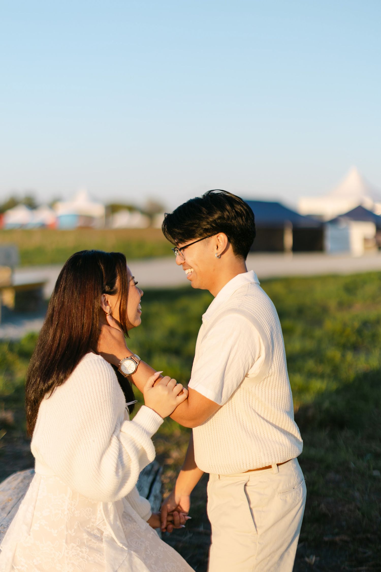 Couple laughing and holding each other affectionately in a grassy field during a golden hour engagement session.