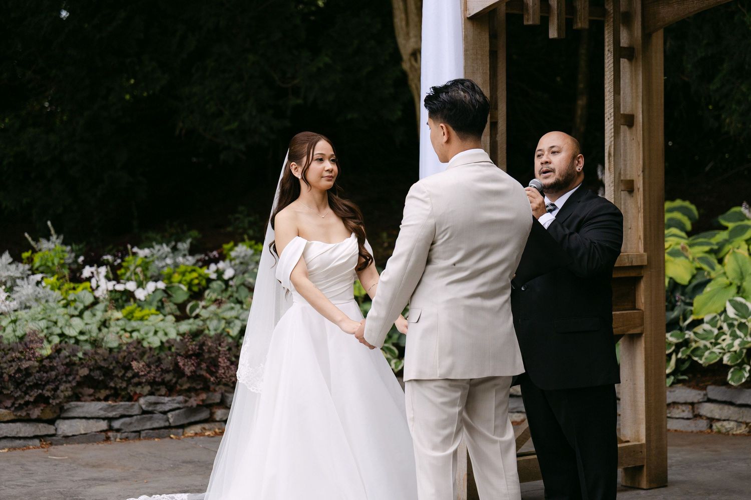 Bride and groom exchange vows outdoors at a garden wedding ceremony with an officiant.