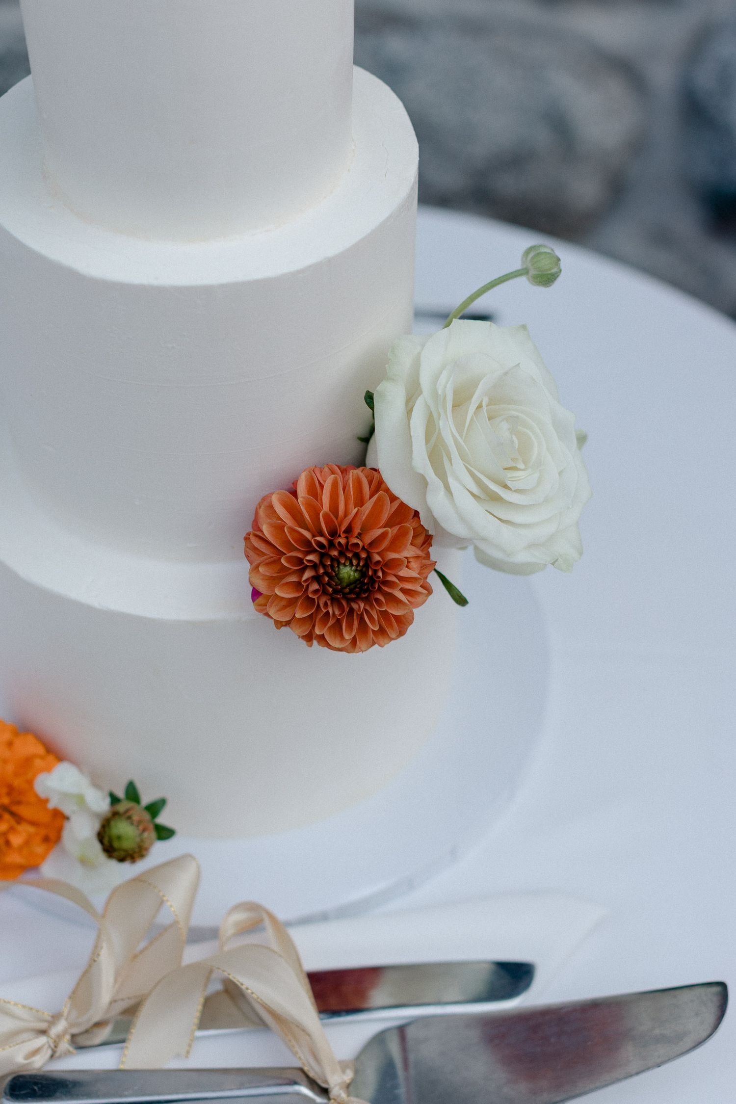 White wedding cake decorated with fresh orange dahlias and white roses on a marble surface.