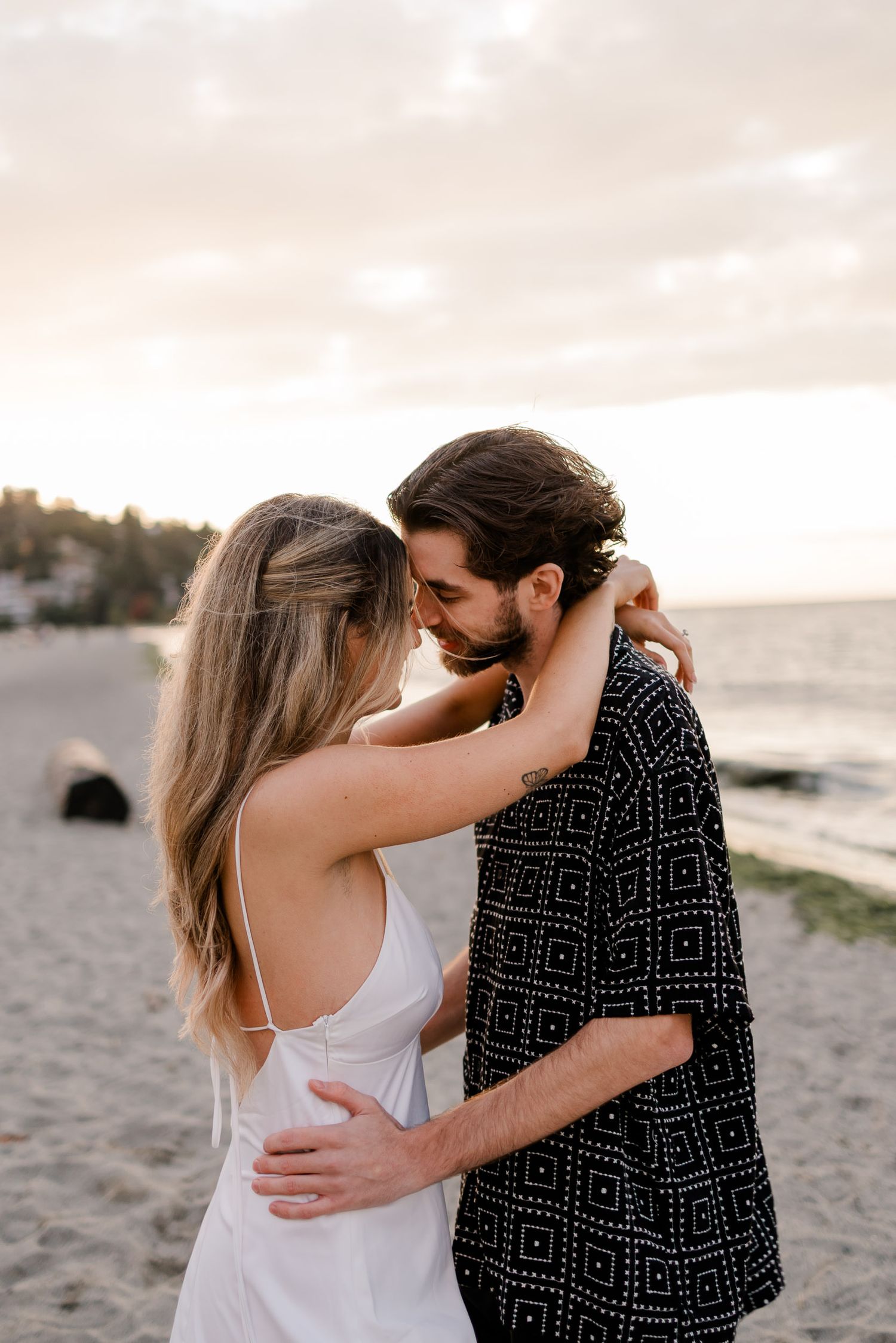 A couple embraces tenderly on a sandy beach at sunset, creating a romantic silhouette against the ocean backdrop.