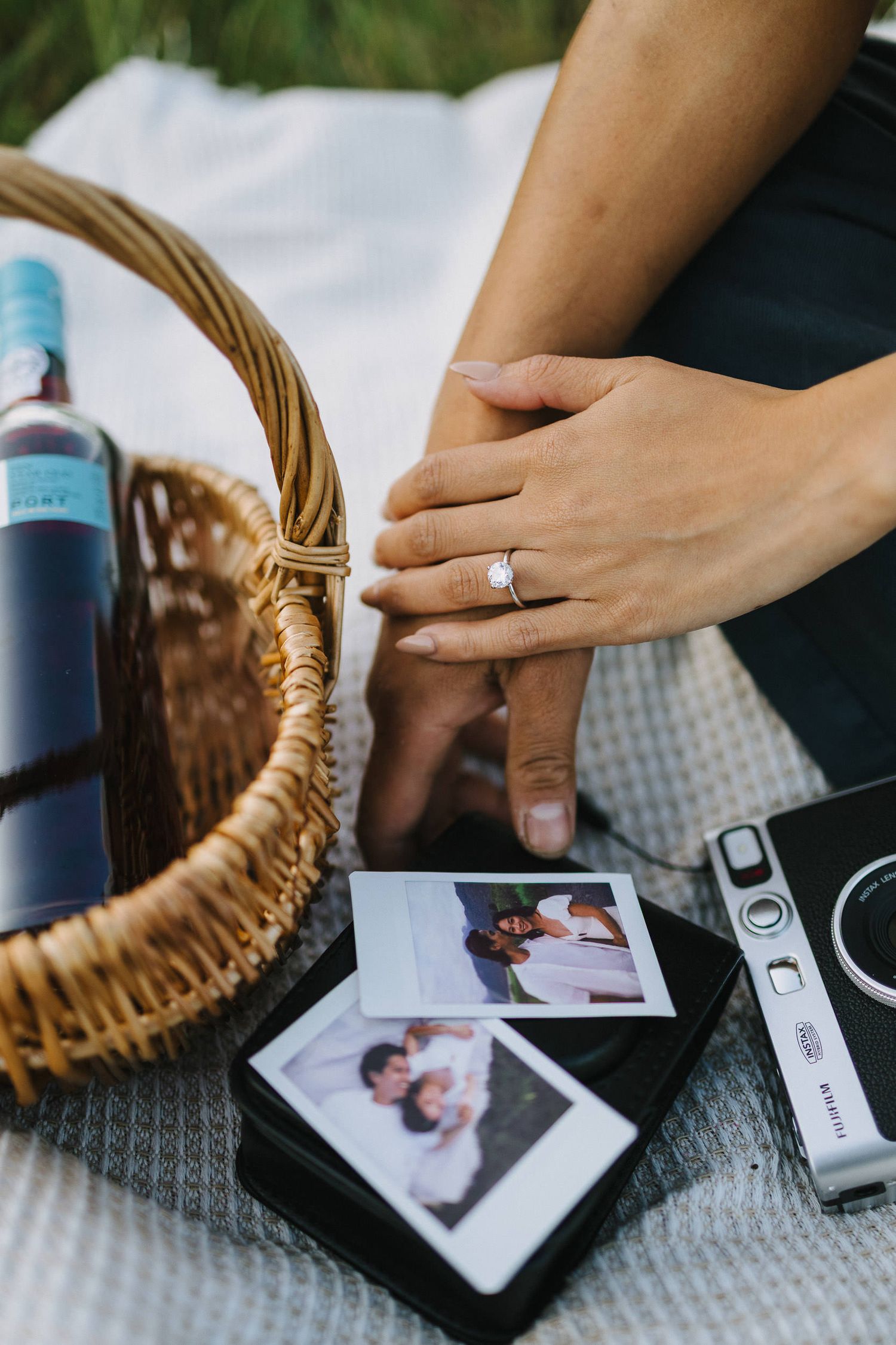 Hand arranges polaroid photos and decorative items with a woven basket on a textured gray surface.