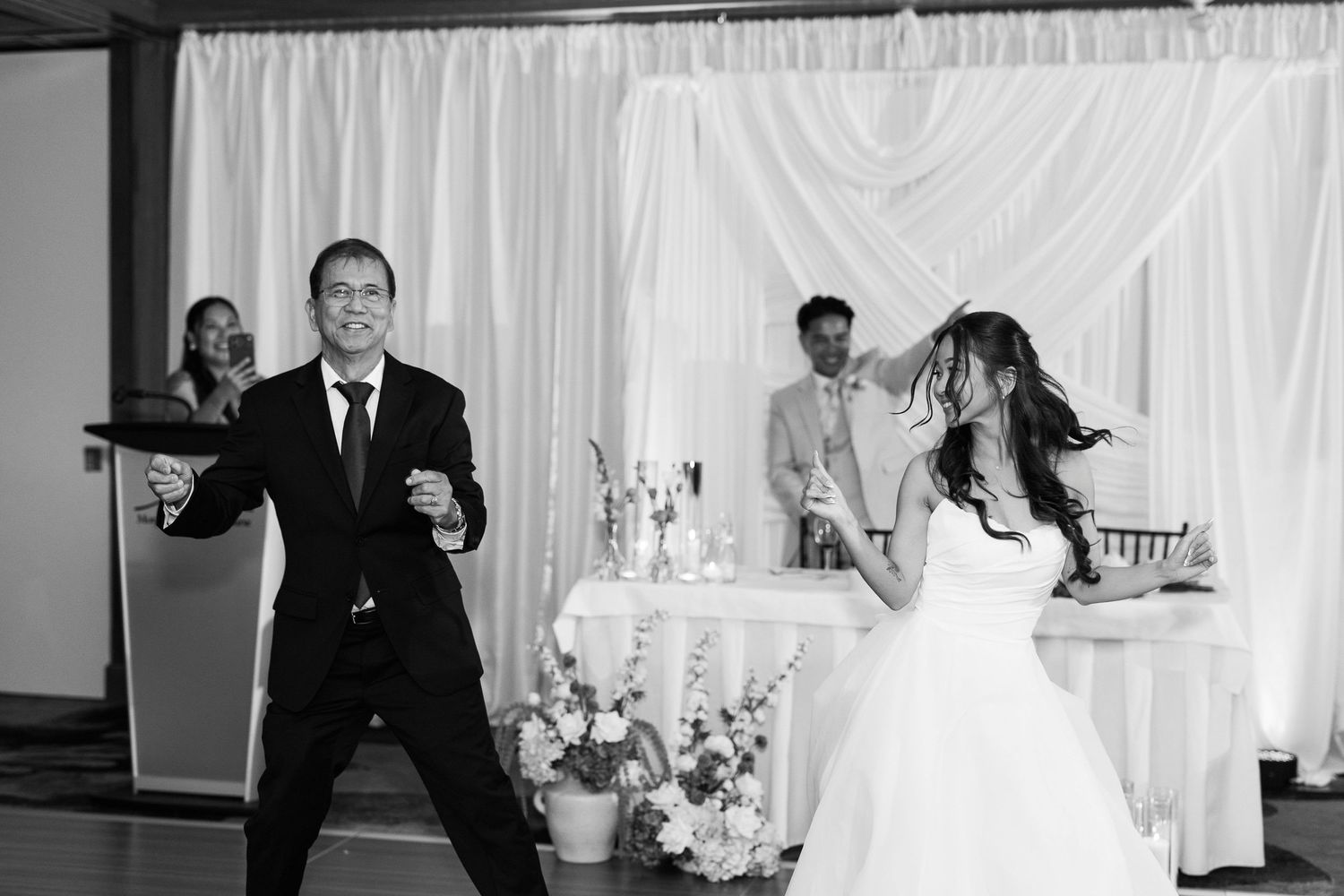 Black and white photo of a bride and groom sharing their first dance at a wedding reception.
