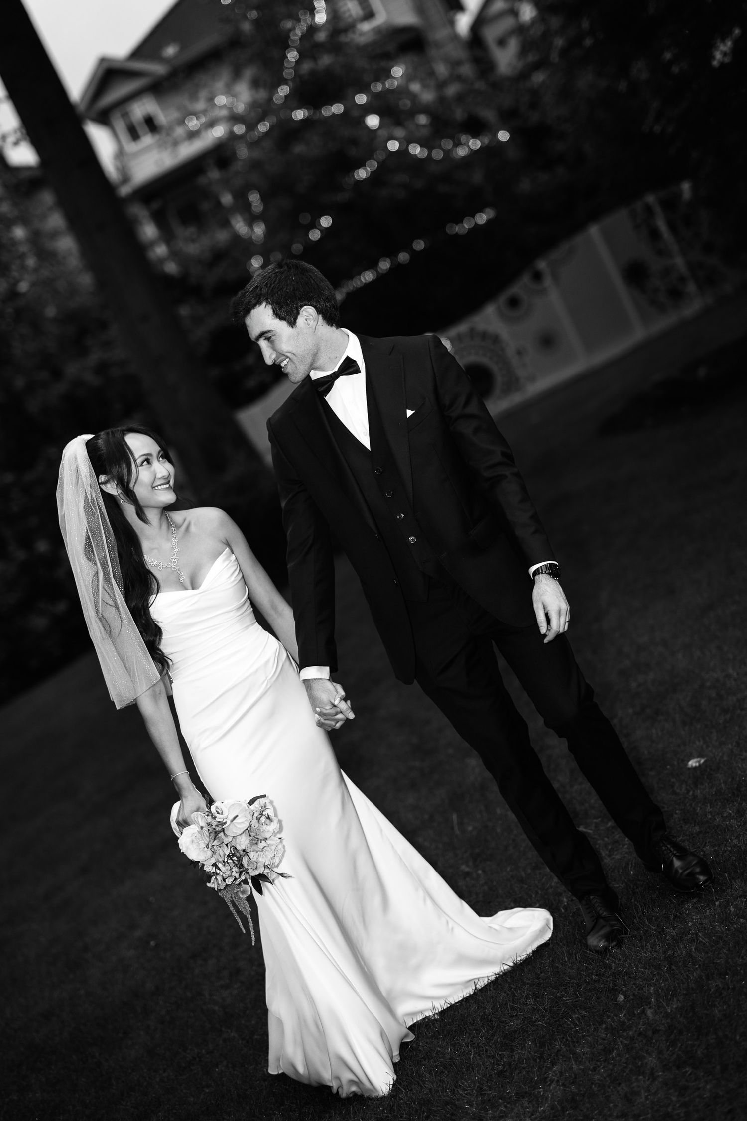 Black and white photo of bride and groom walking hand in hand with wedding bouquet.