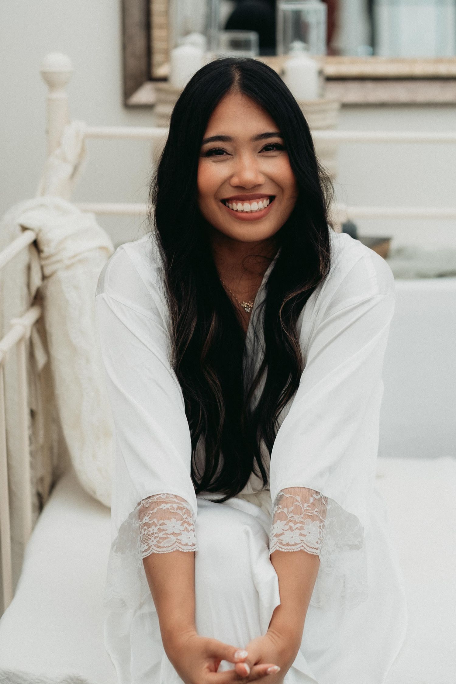 Woman in white lace dress sitting and smiling joyfully in a light and airy indoor setting.