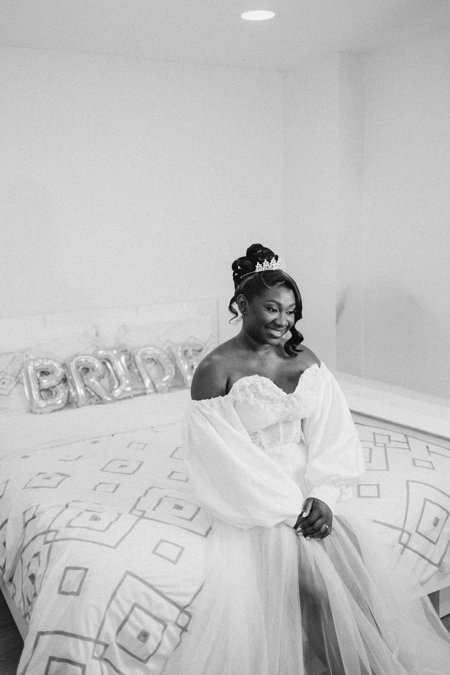 Black and white photo of bride in flowing white dress with balloon sleeves in minimalist room setting.