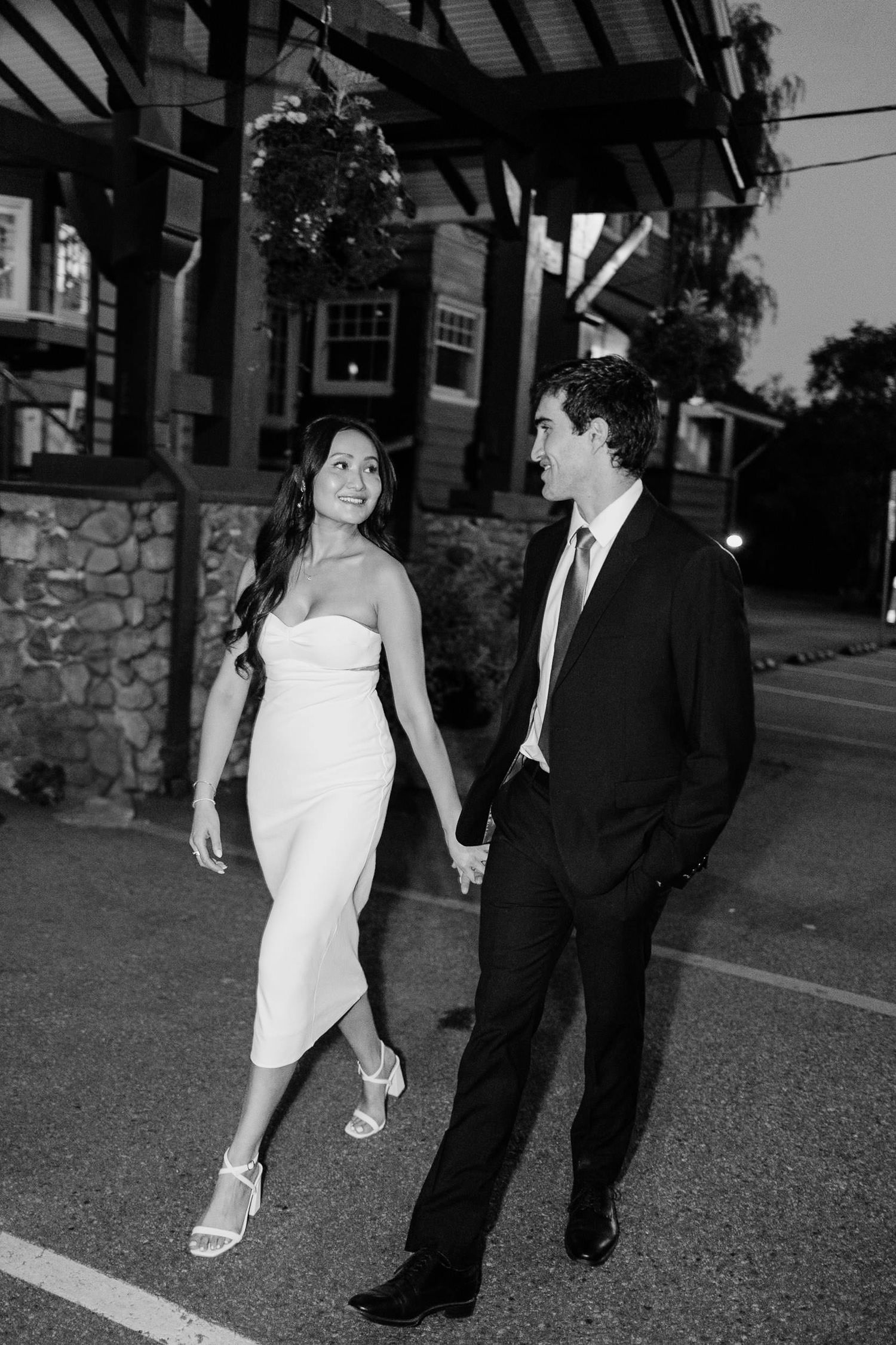 Black and white photo of a couple walking together at dusk, with the woman in a white dress and man in dark suit.
