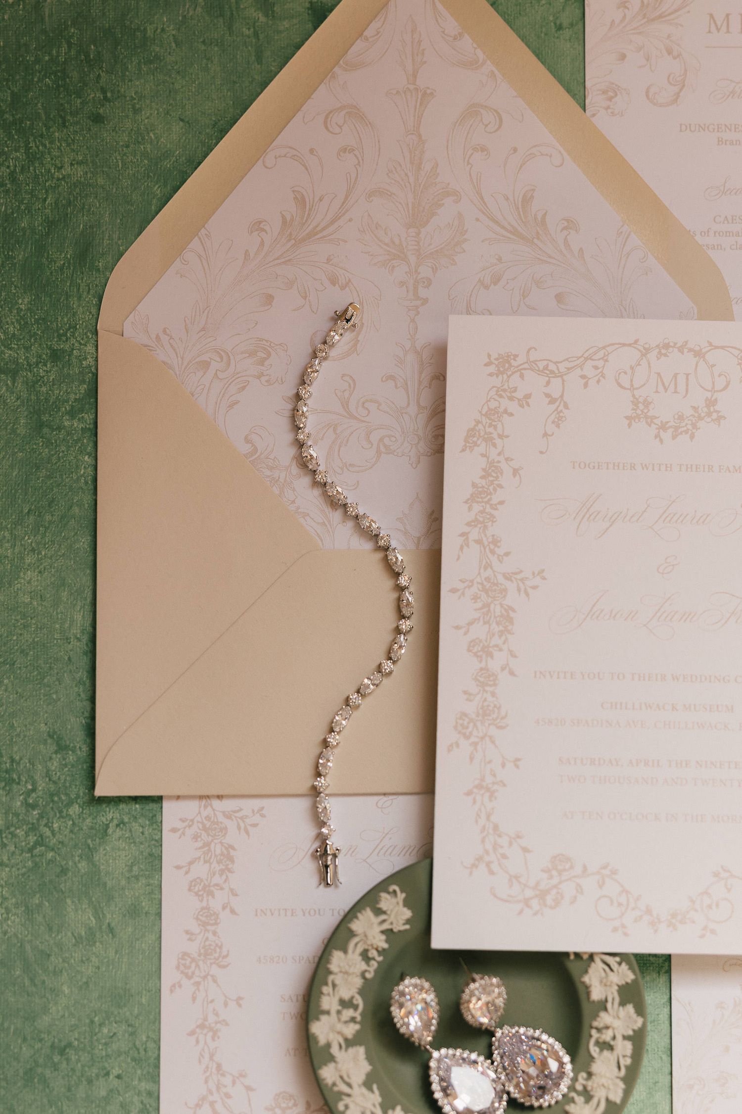 Elegant wedding invitations with blush envelopes and delicate floral designs laid out on a green textured surface.