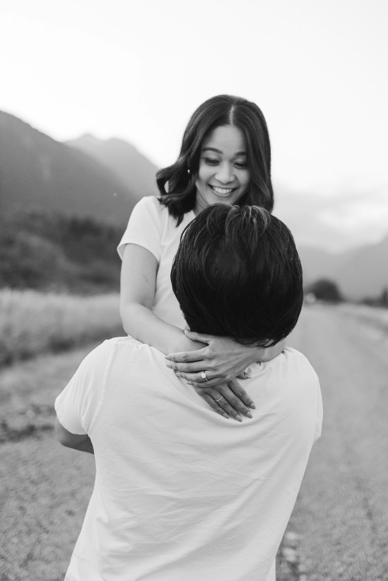 Black and white portrait of a smiling woman embracing a man during an engagement photo session in the mountains.