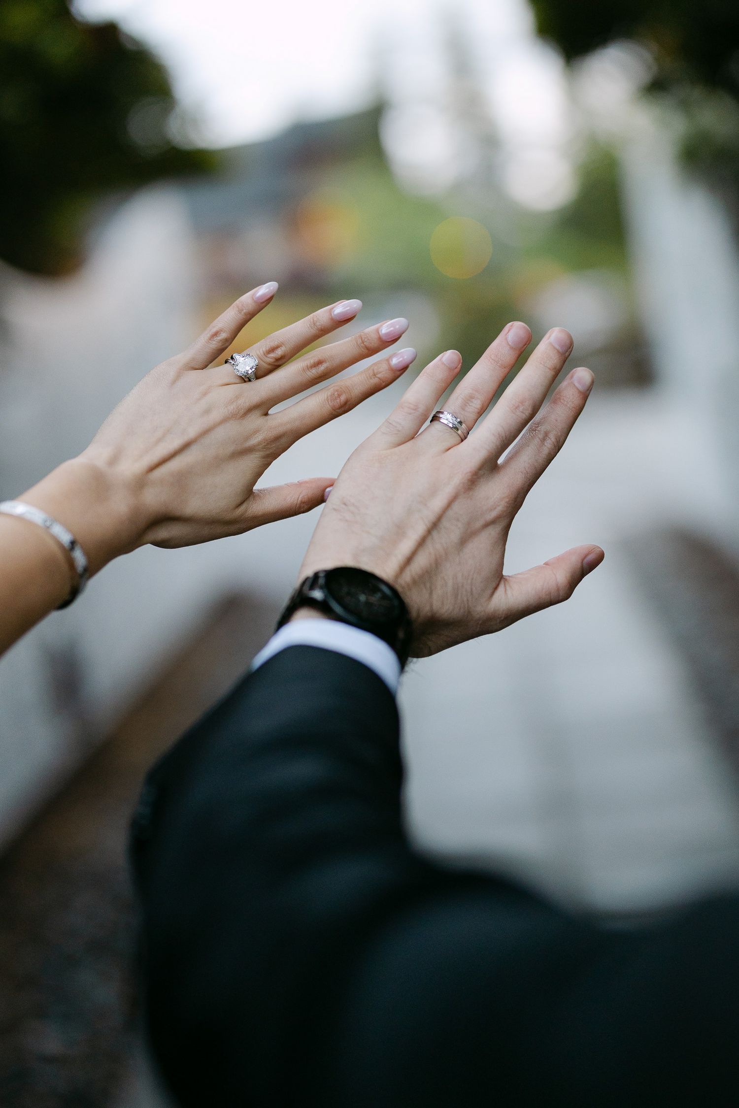 Newlyweds displaying wedding rings, bride with French manicure and groom wearing black watch.