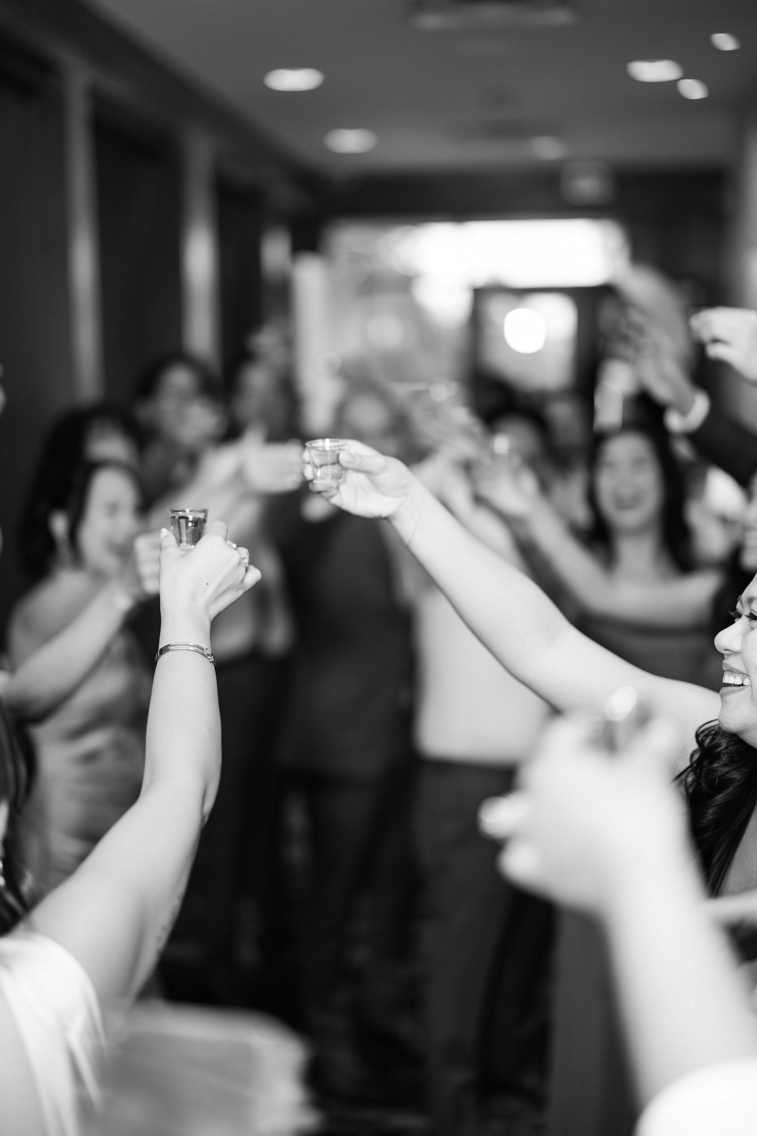 Black and white photo of wedding guests raising glasses in a toast during a celebratory reception.