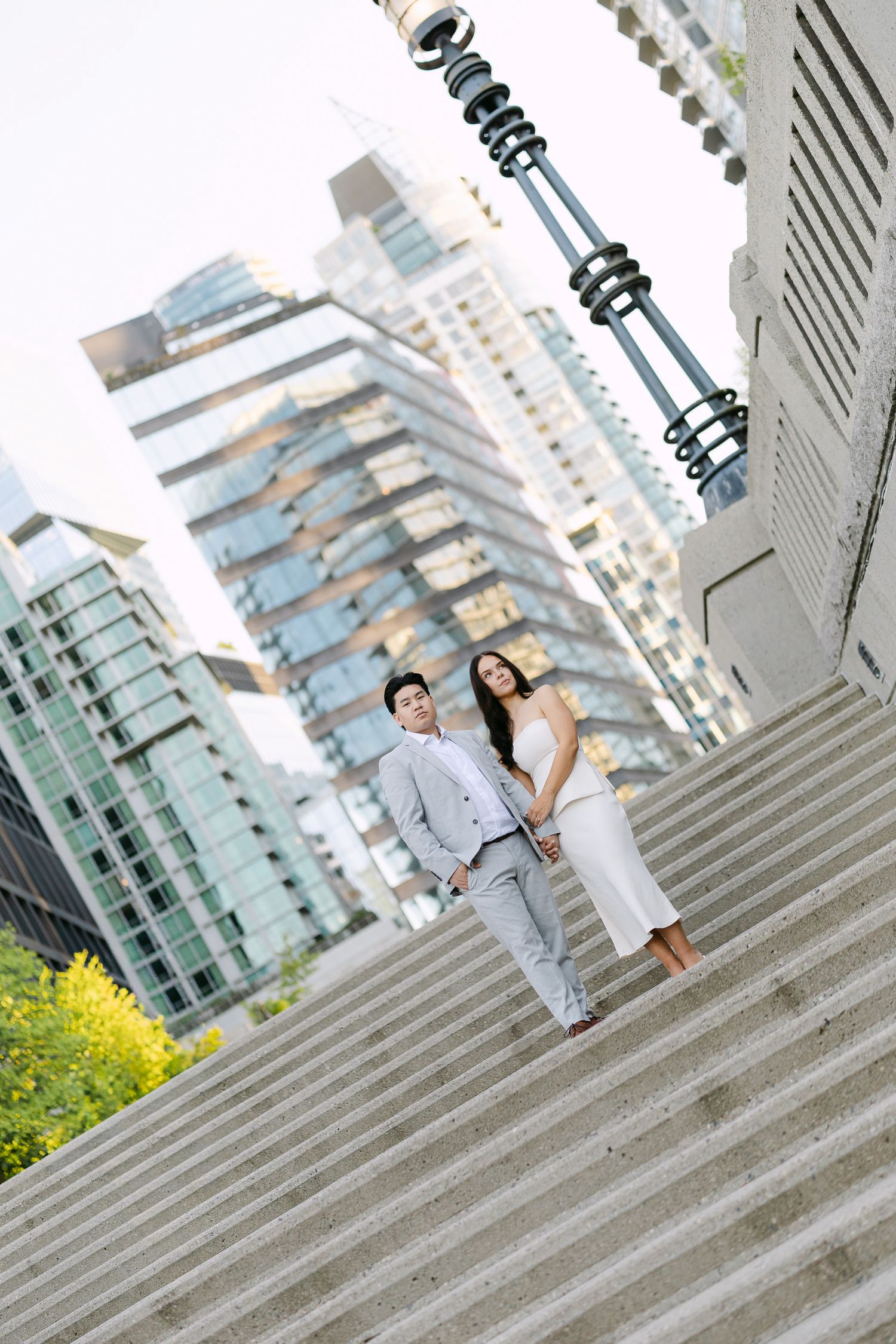 Engaged couple standing close on outdoor stairs with modern high-rise buildings rising behind them in an urban engagement photo.