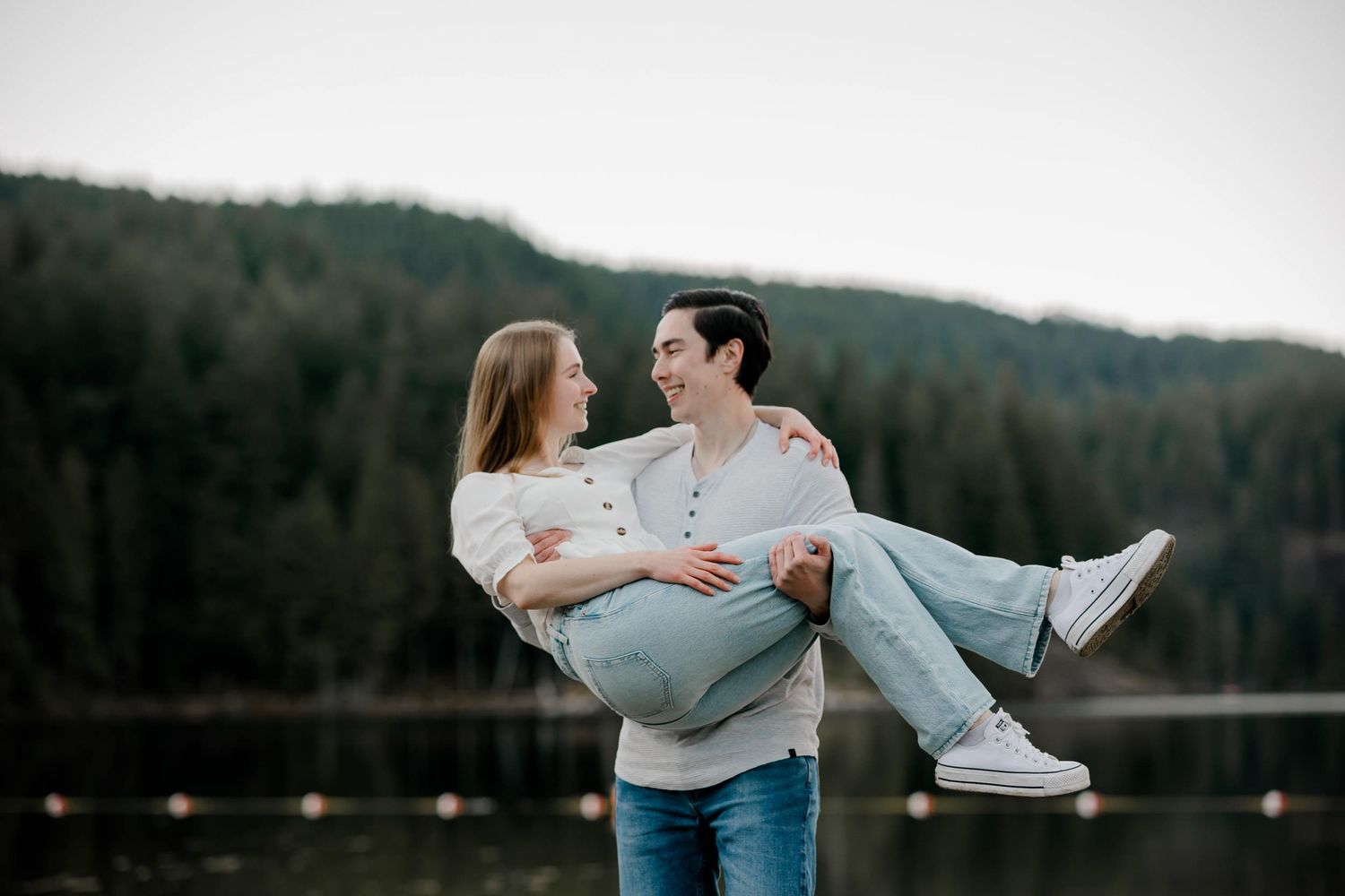 Couple in casual wear dancing and spinning together in front of a scenic mountain lake view at sunset.
