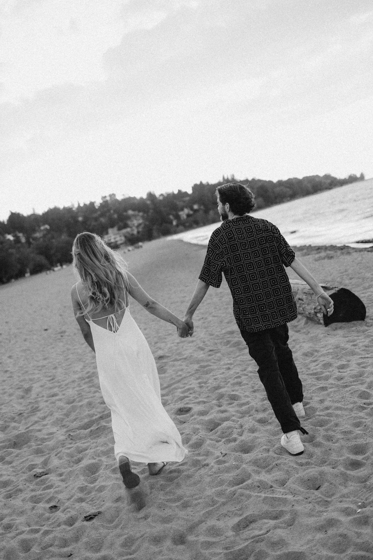 A couple runs and plays together on a sandy beach in black and white photography.