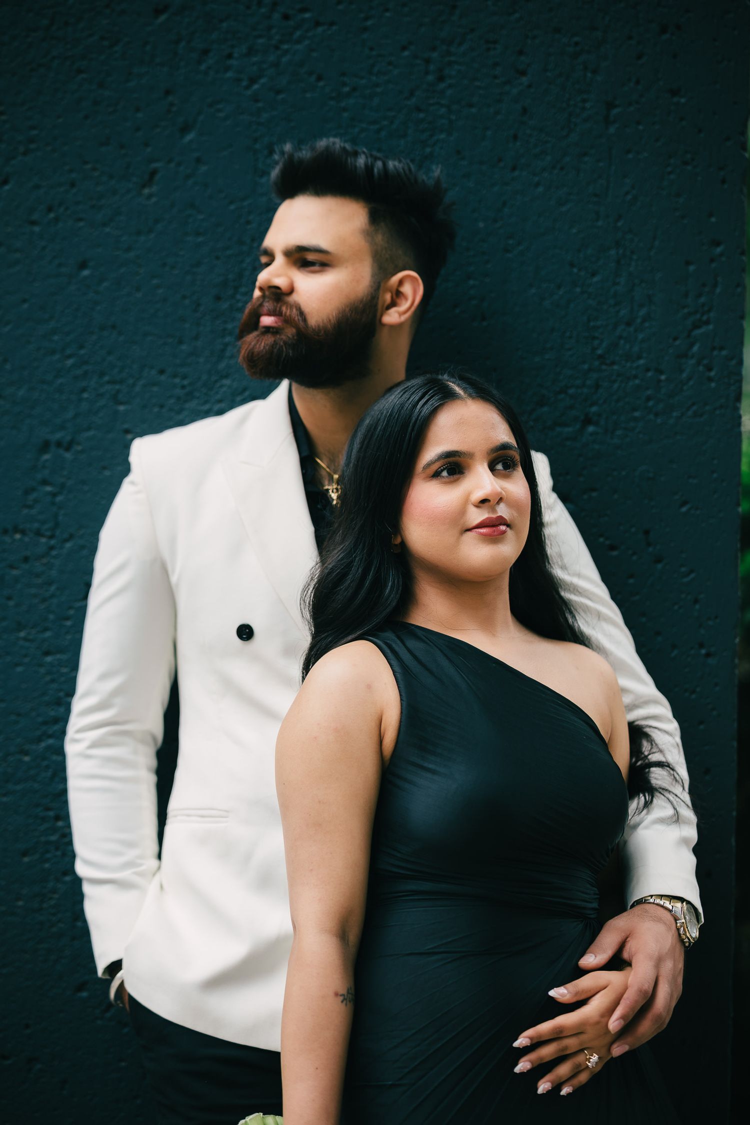 A couple in contrasting black and white outfits pose intimately against a dark wall in a romantic photoshoot series.