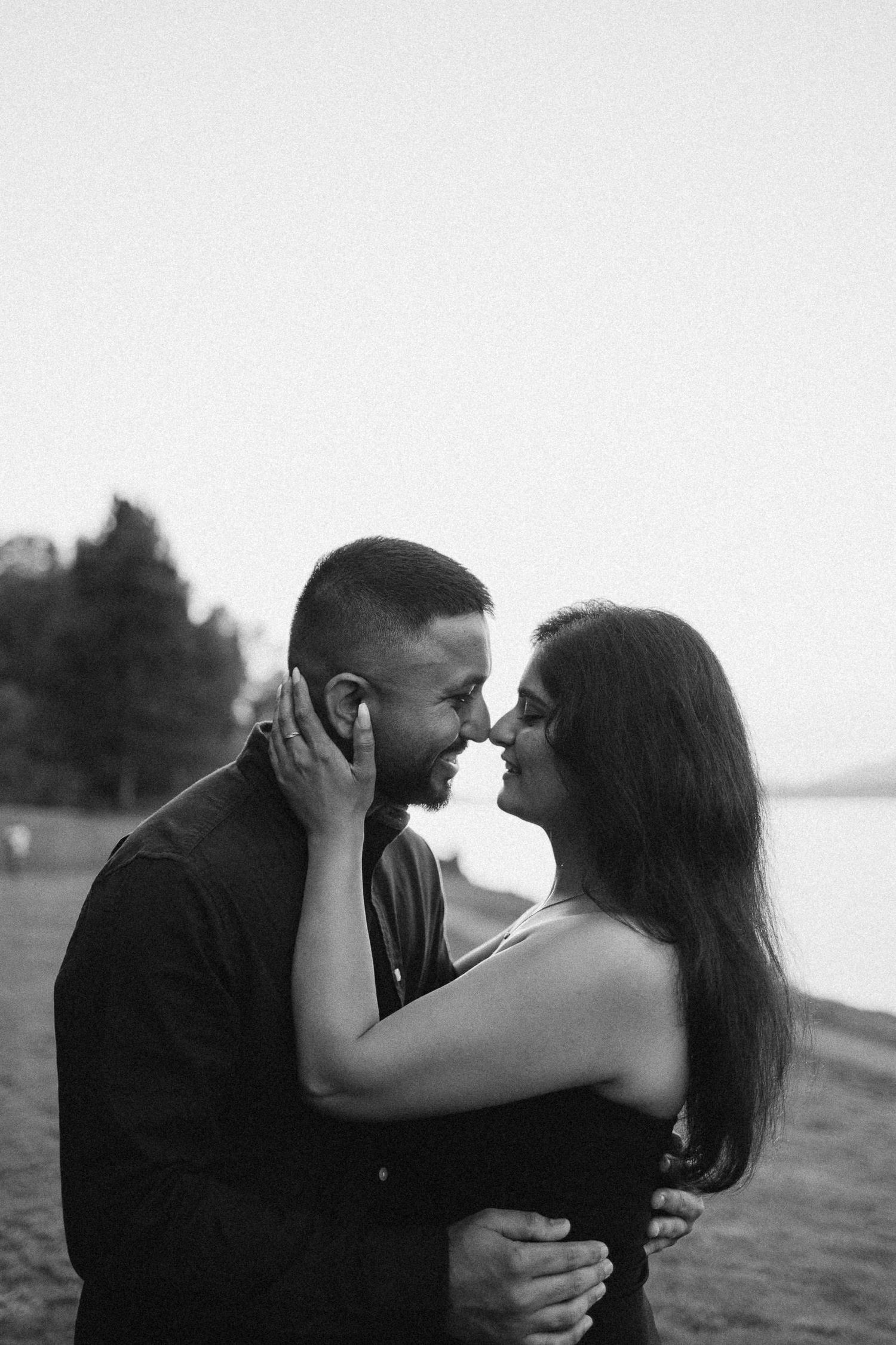 A romantic couple embraces in black and white silhouette against a natural outdoor backdrop during a photoshoot.