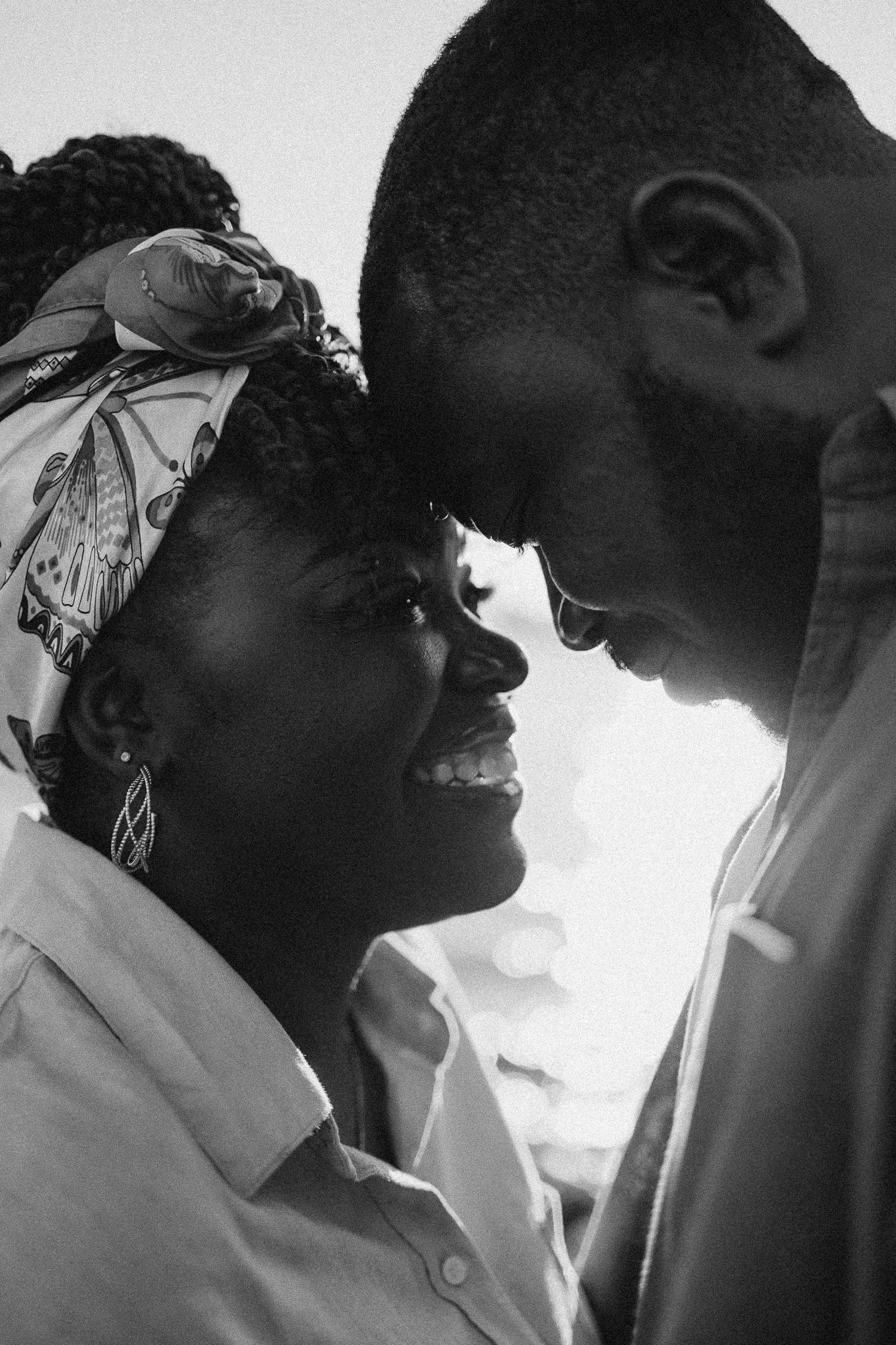 A tender black and white portrait of a couple sharing an intimate moment, with one wearing a patterned headscarf.
