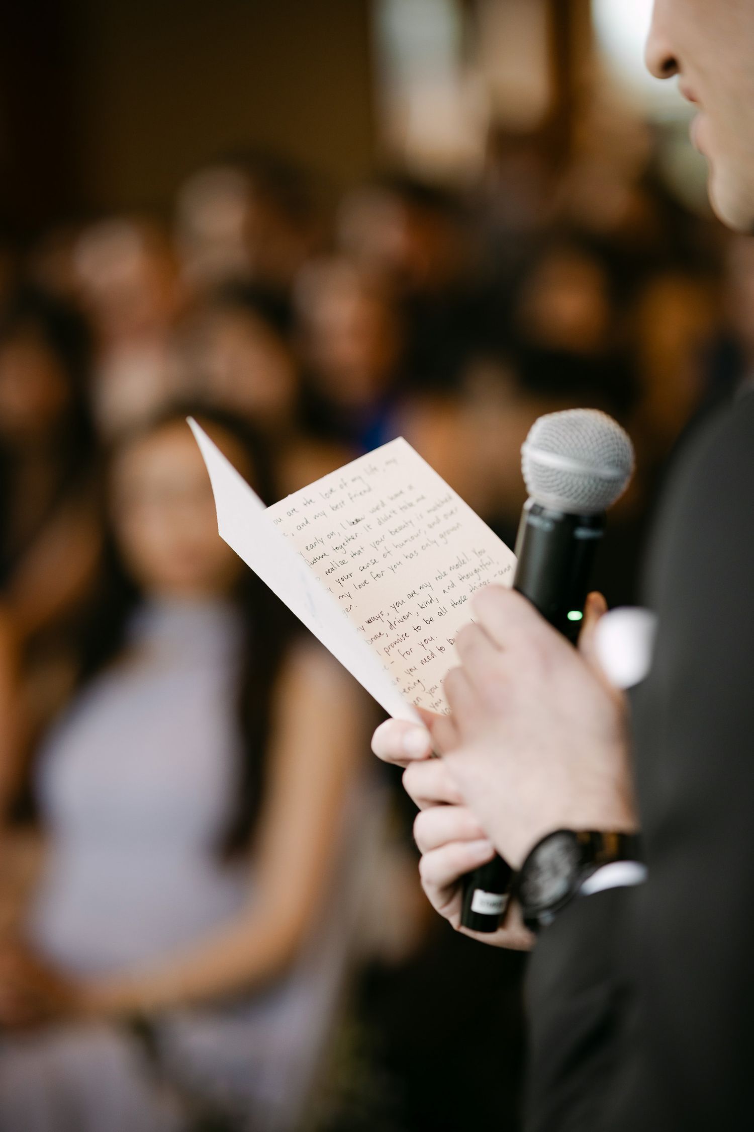 Person holding a microphone and handwritten notes while giving a speech at a wedding ceremony.