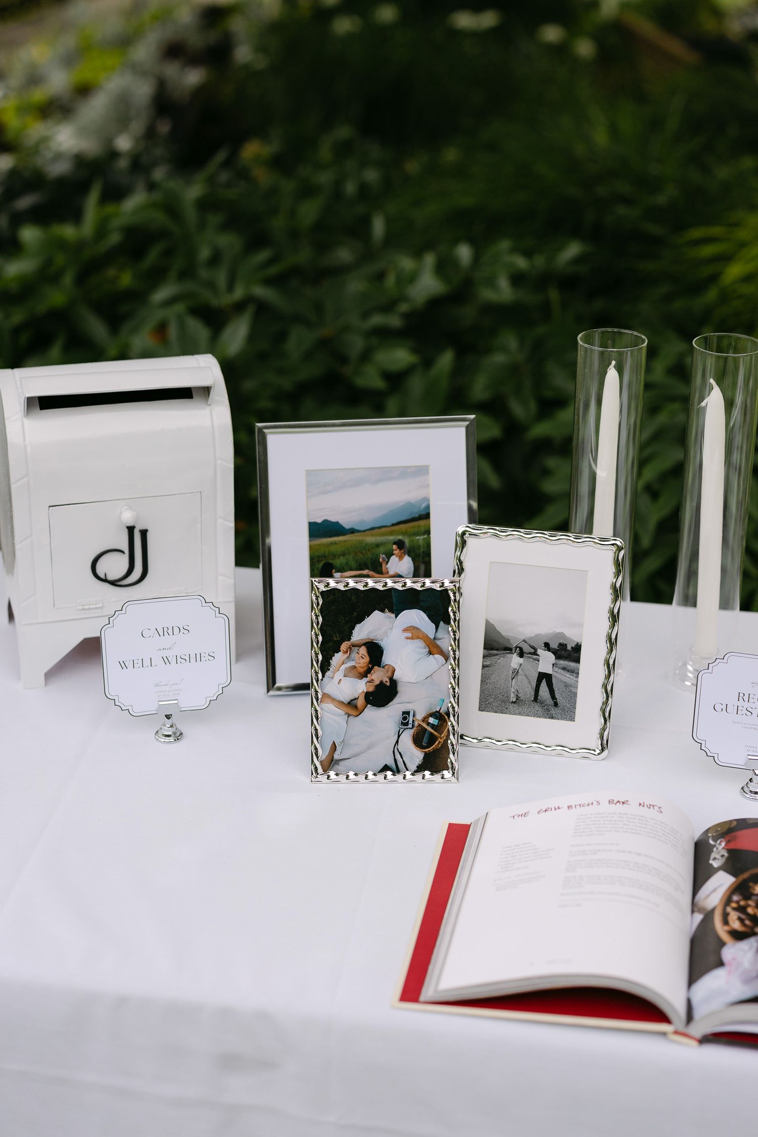 Wedding gift table with white card box, framed couple photos, candles, and open guest book on white linen tablecloth.