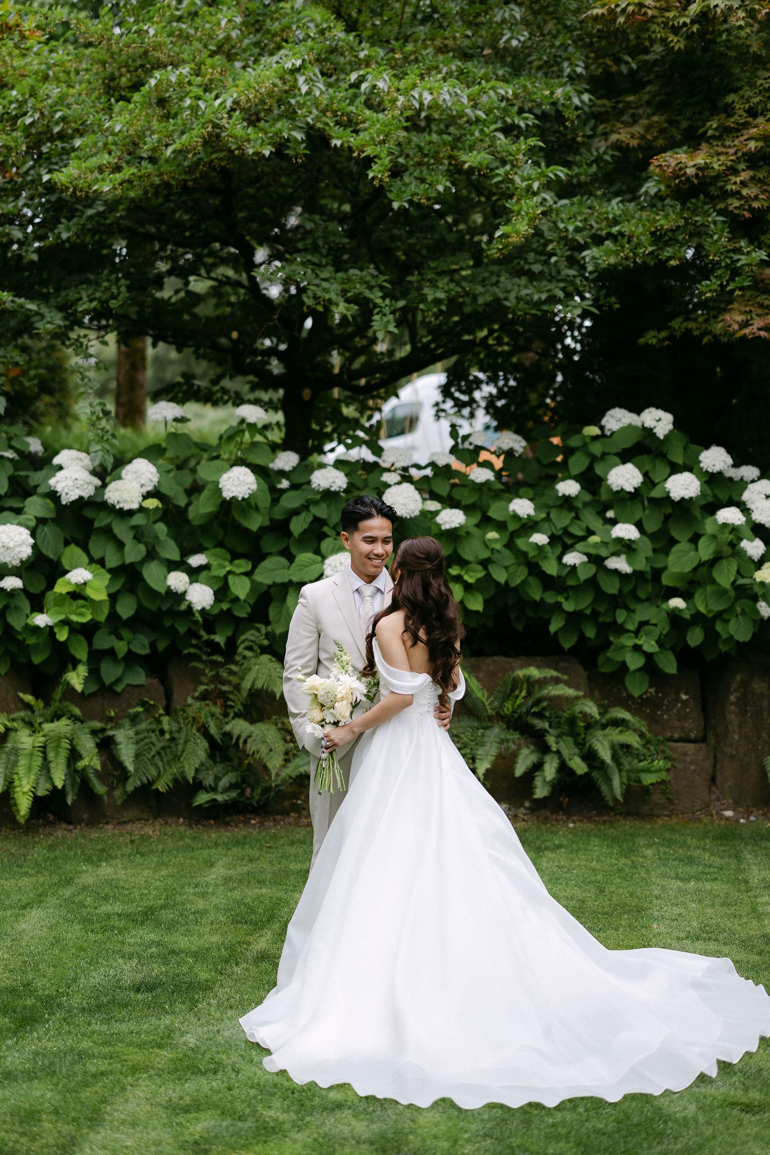 Bride and groom share a romantic moment in a lush garden with white hydrangeas, bride wearing an elegant ball gown.