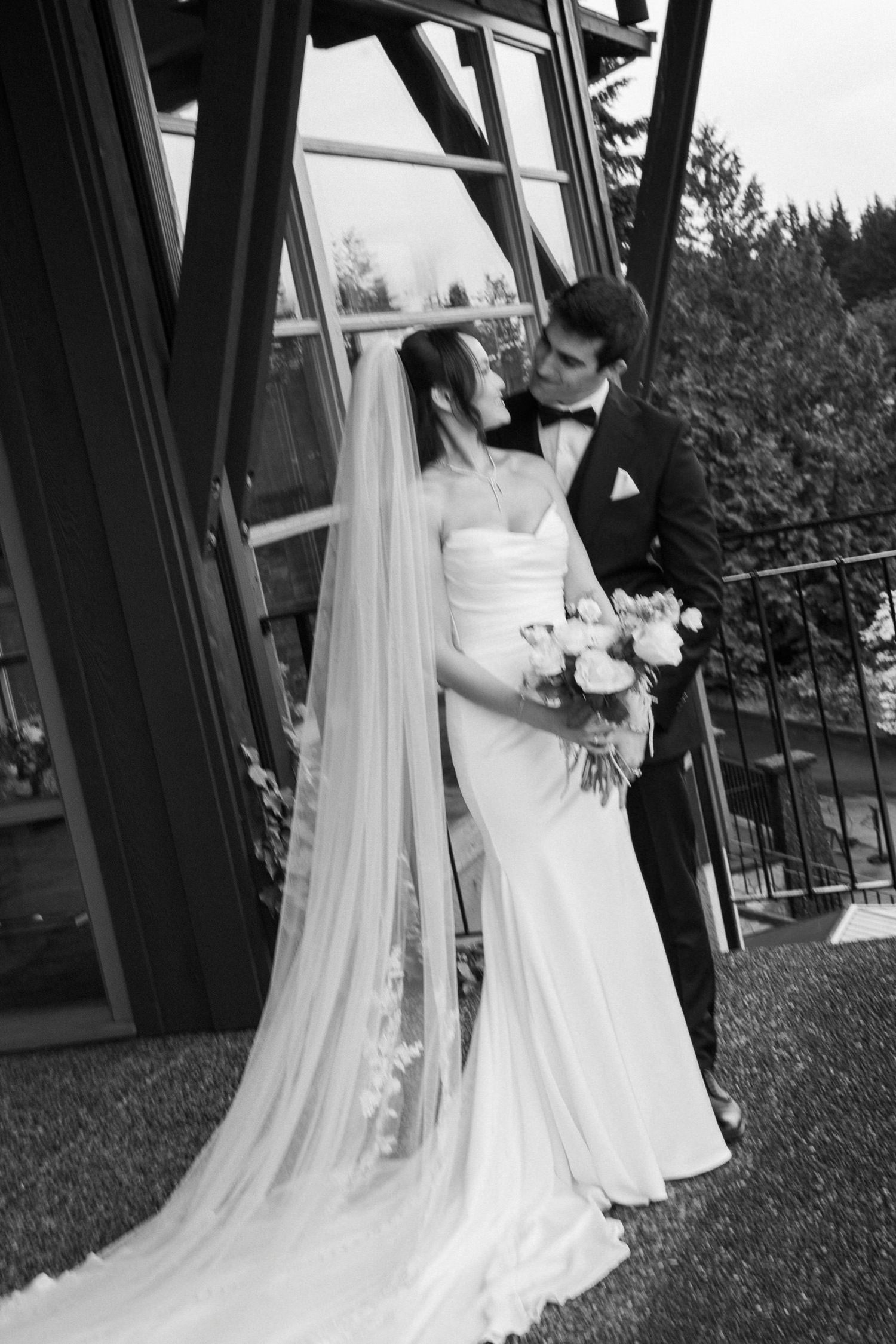 Black and white photo of bride and groom sharing a kiss outside a rustic venue.