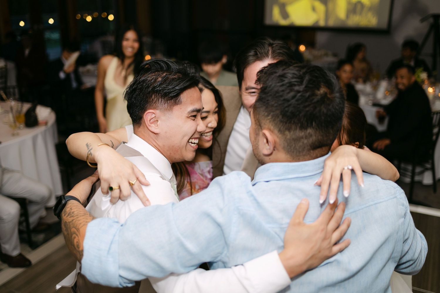 Friends sharing a warm group hug and laughing together at an elegant wedding reception celebration.