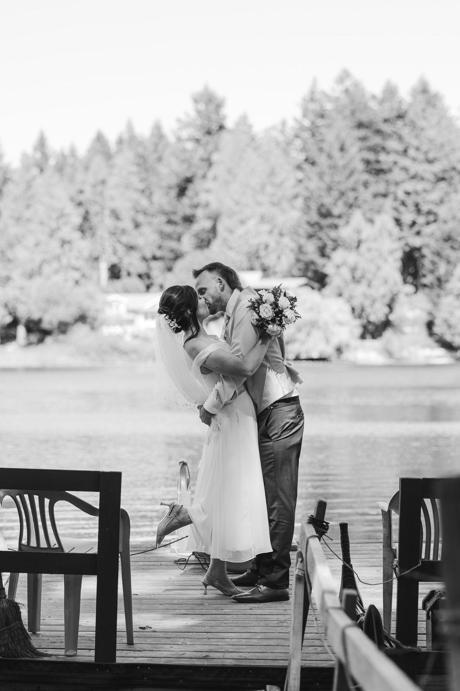 Black and white photo of a couple sharing a tender moment on a lakeside dock.