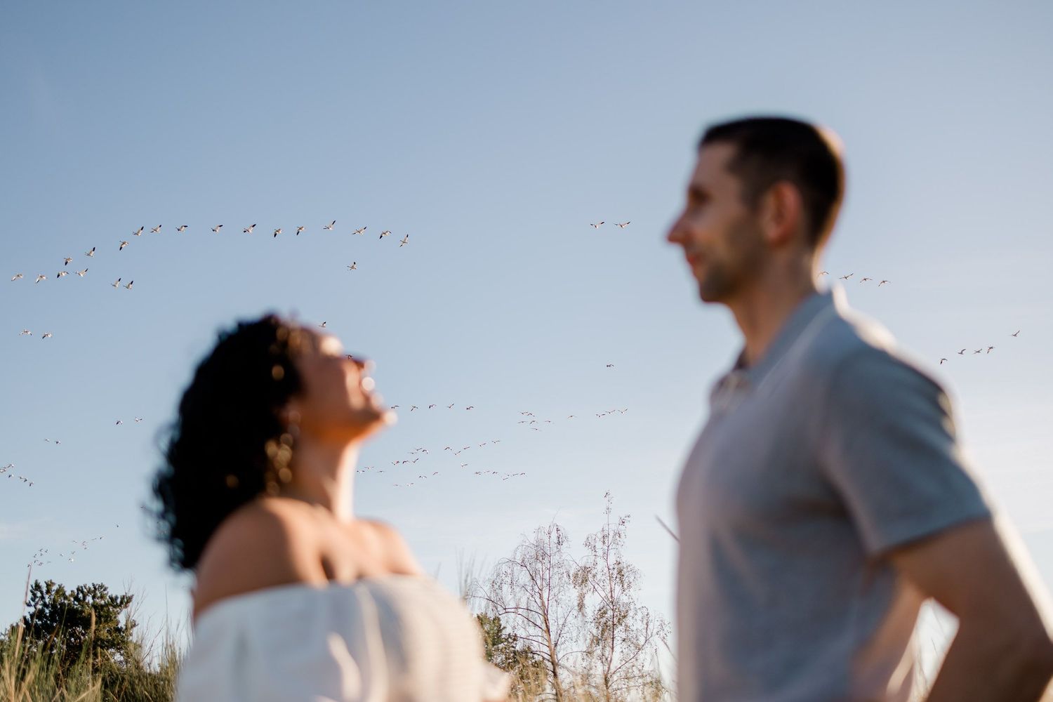 A couple embraces in silhouette against a bright sky during a romantic outdoor photoshoot.
