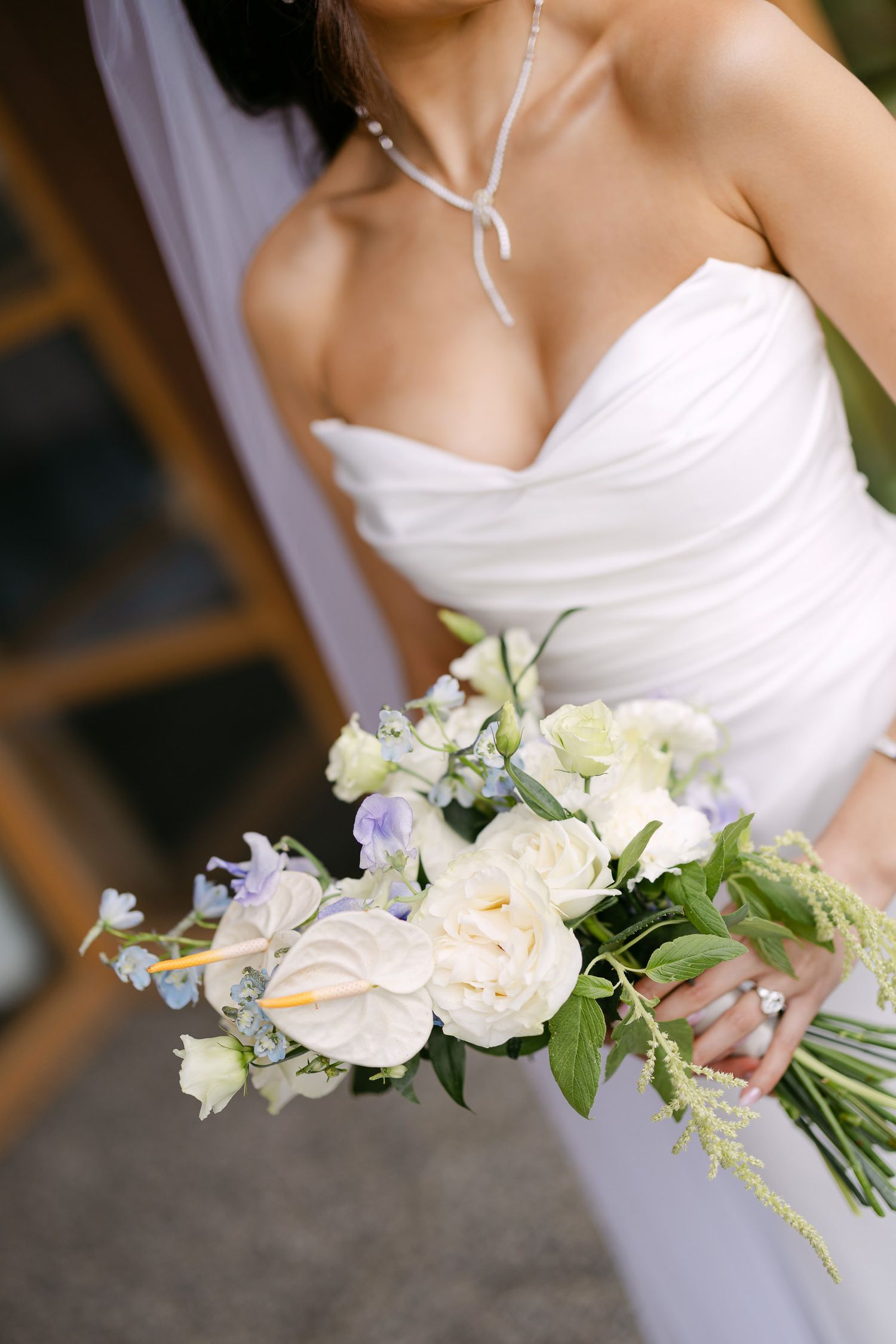 Close-up of bridal bouquet featuring white roses, anthurium, and soft blue flowers with green accents.