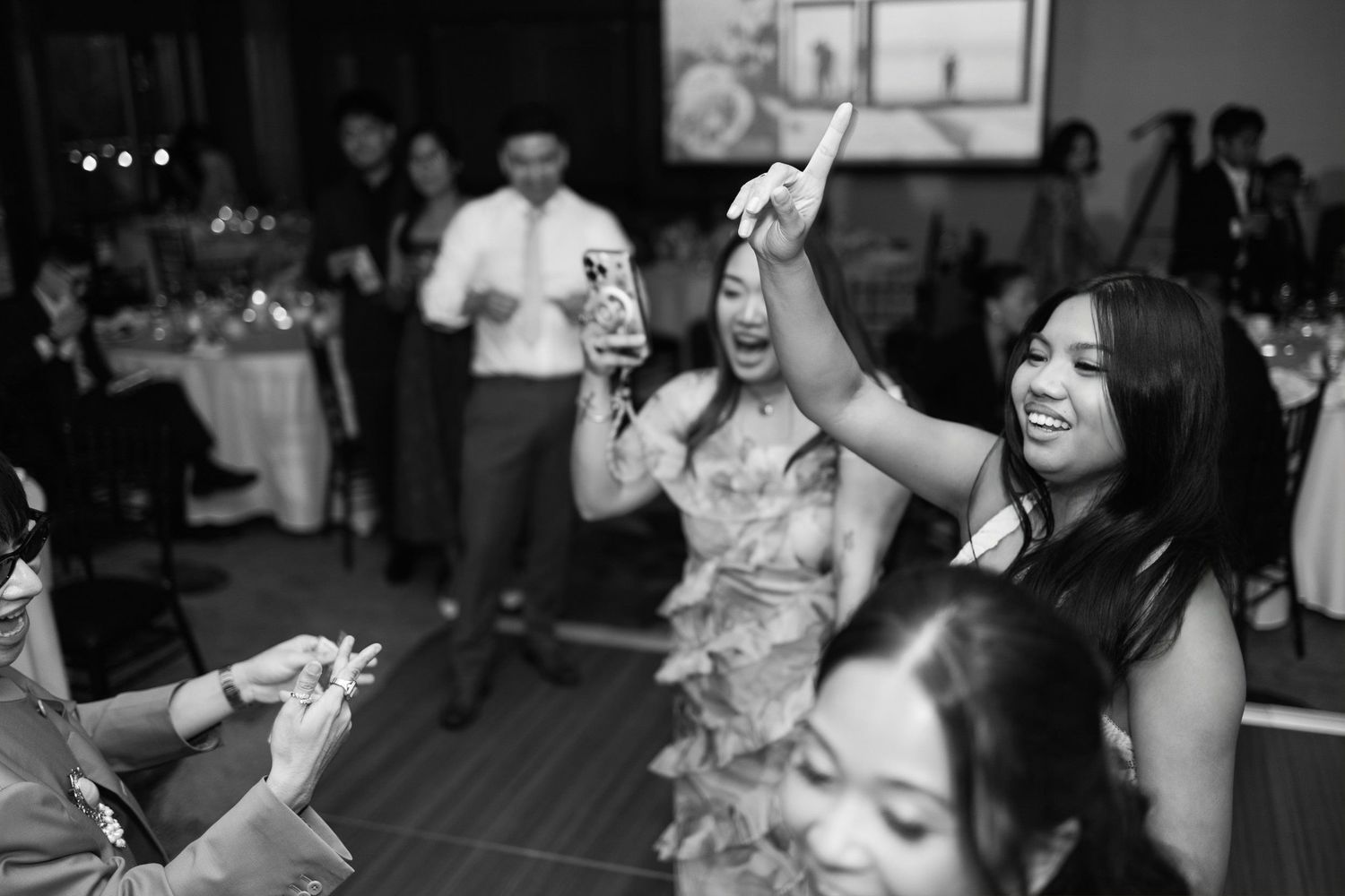 Guests dancing and laughing joyfully at a wedding reception in black and white photo.