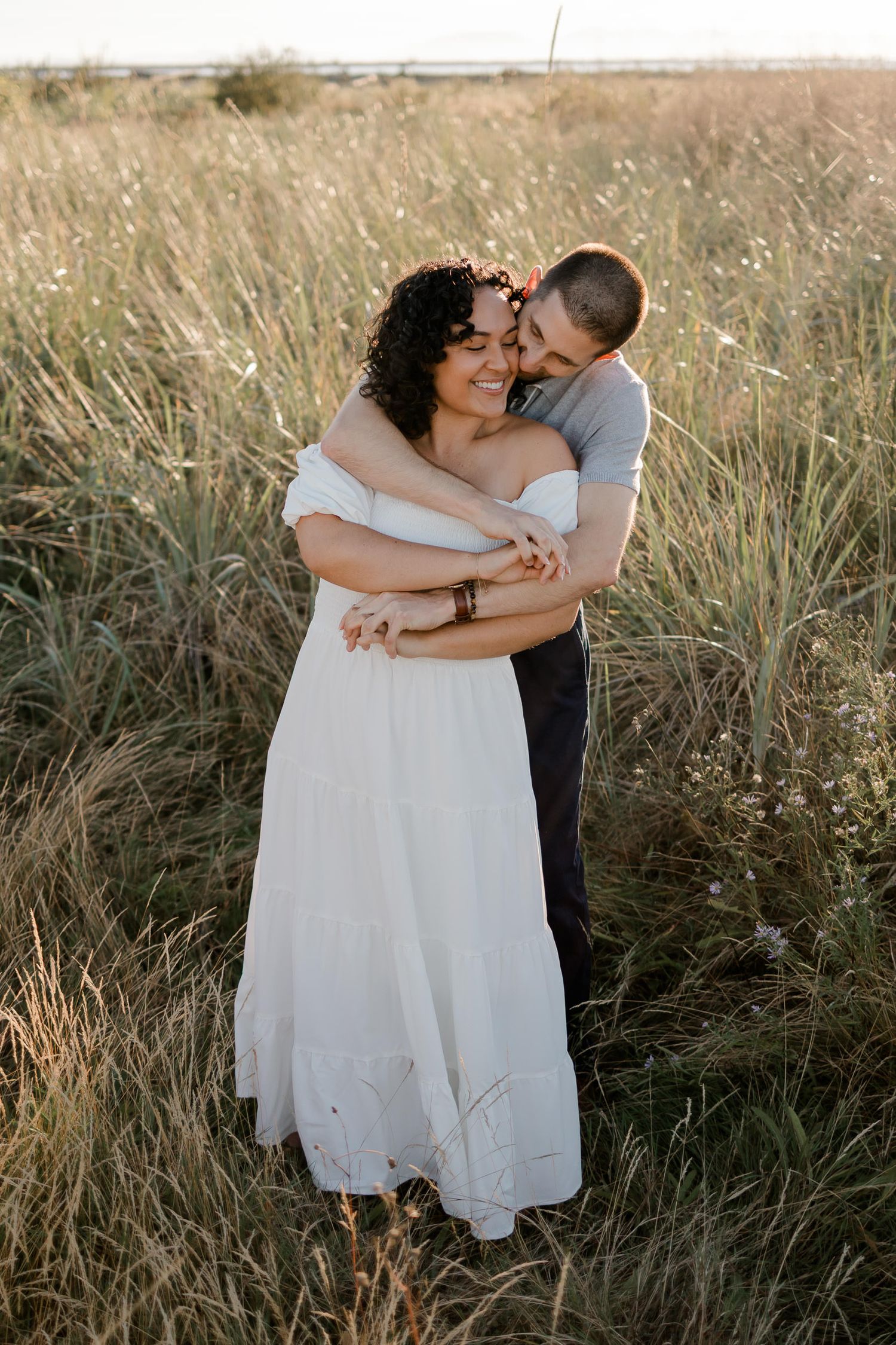 Intimate couple embracing in golden sunlit field with tall grass.