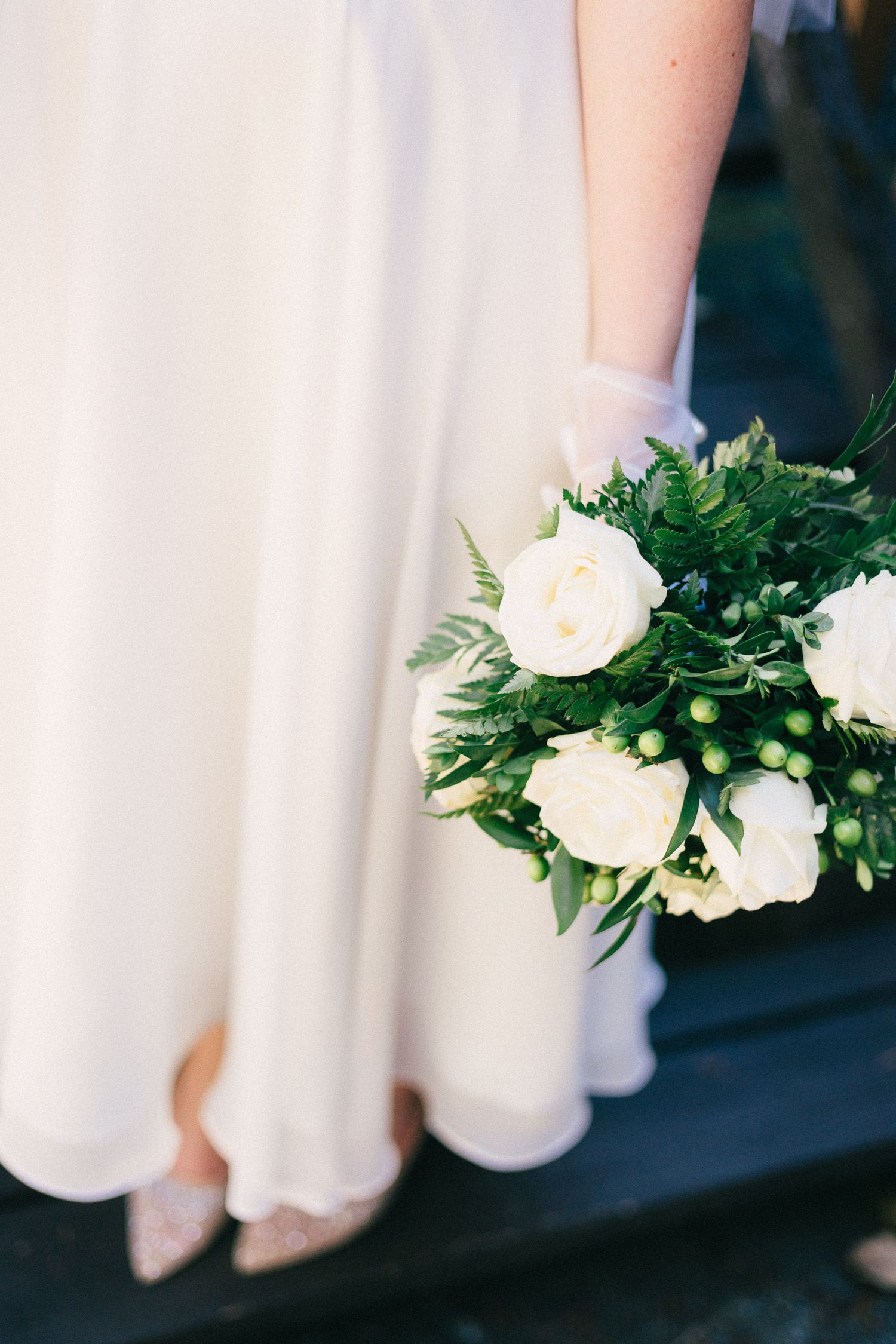 Close-up view of white roses and greenery bouquets held by bridesmaids in light colored dresses.