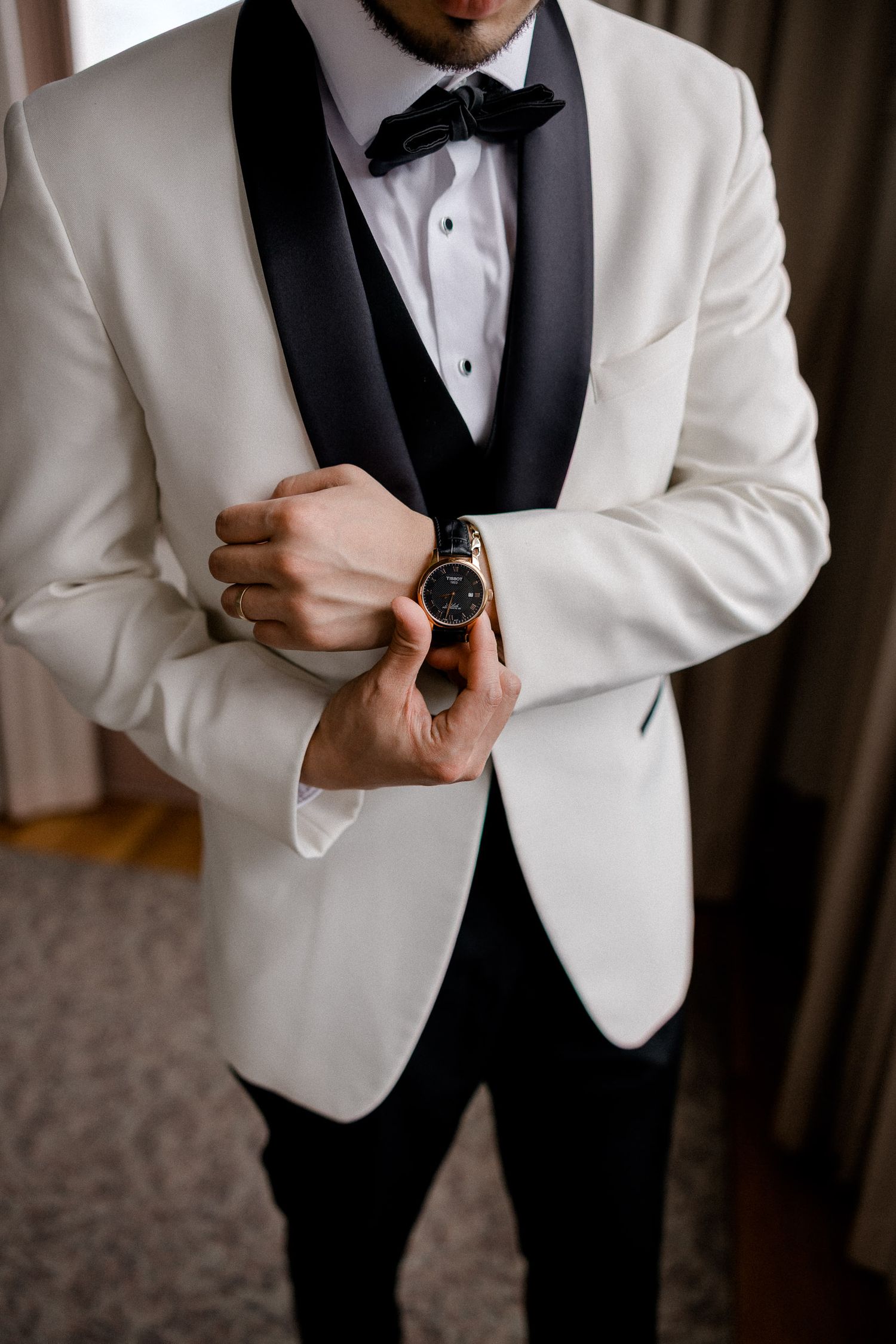 Close-up details of a groom adjusting cufflinks while wearing a crisp white tuxedo jacket.