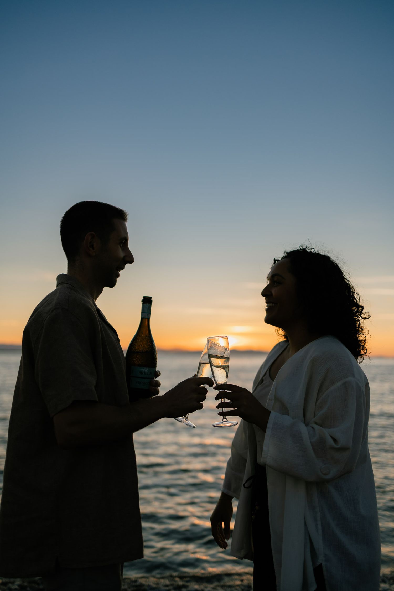 Silhouettes of people sharing drinks against a sunset ocean backdrop.