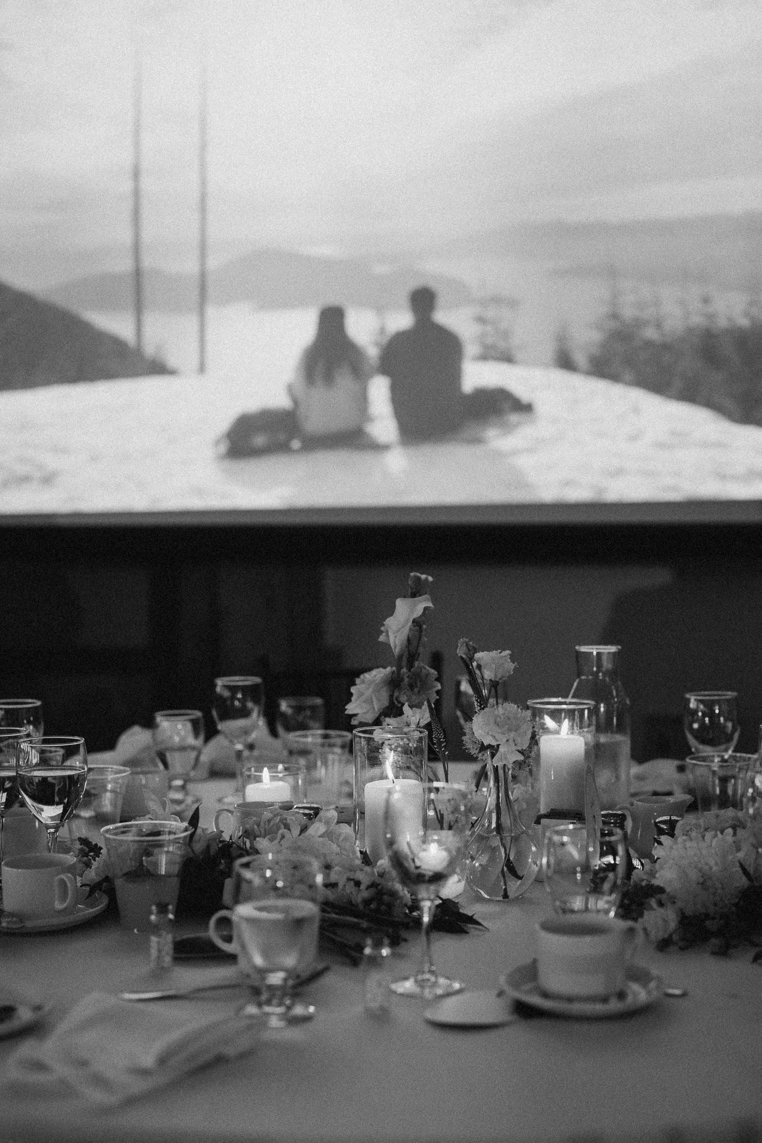Black and white wedding reception table with candles and florals, romantic couple silhouette projected on screen behind.
