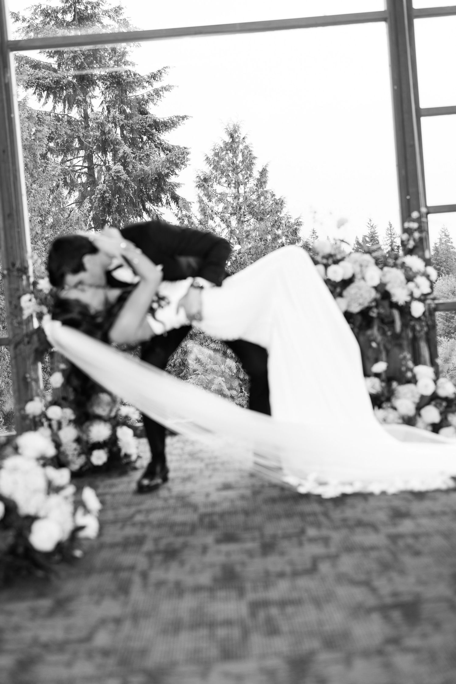 Groom dips bride for romantic kiss at wedding ceremony in black and white photo.