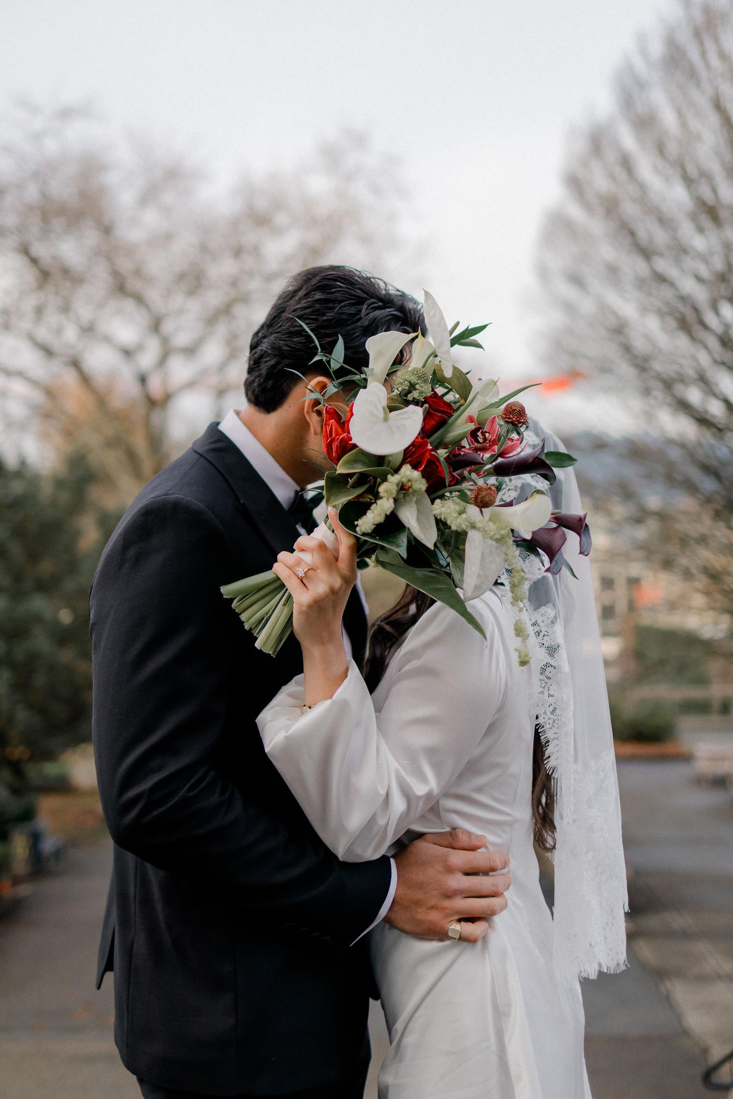A couple shares an intimate moment behind a floral bouquet in a winter outdoor setting.