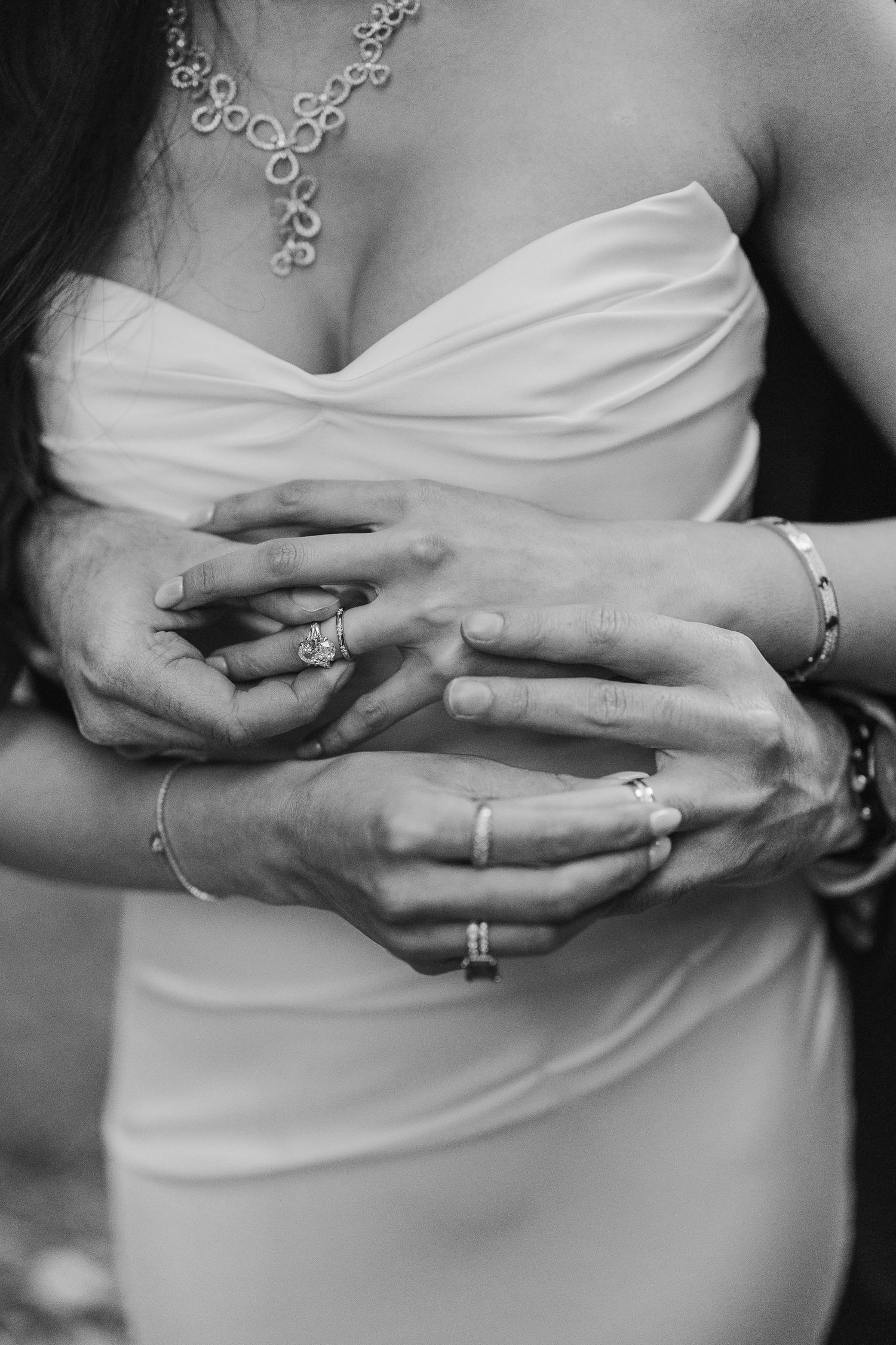 Black and white close-up of bride and groom's hands showing wedding rings and jewelry.