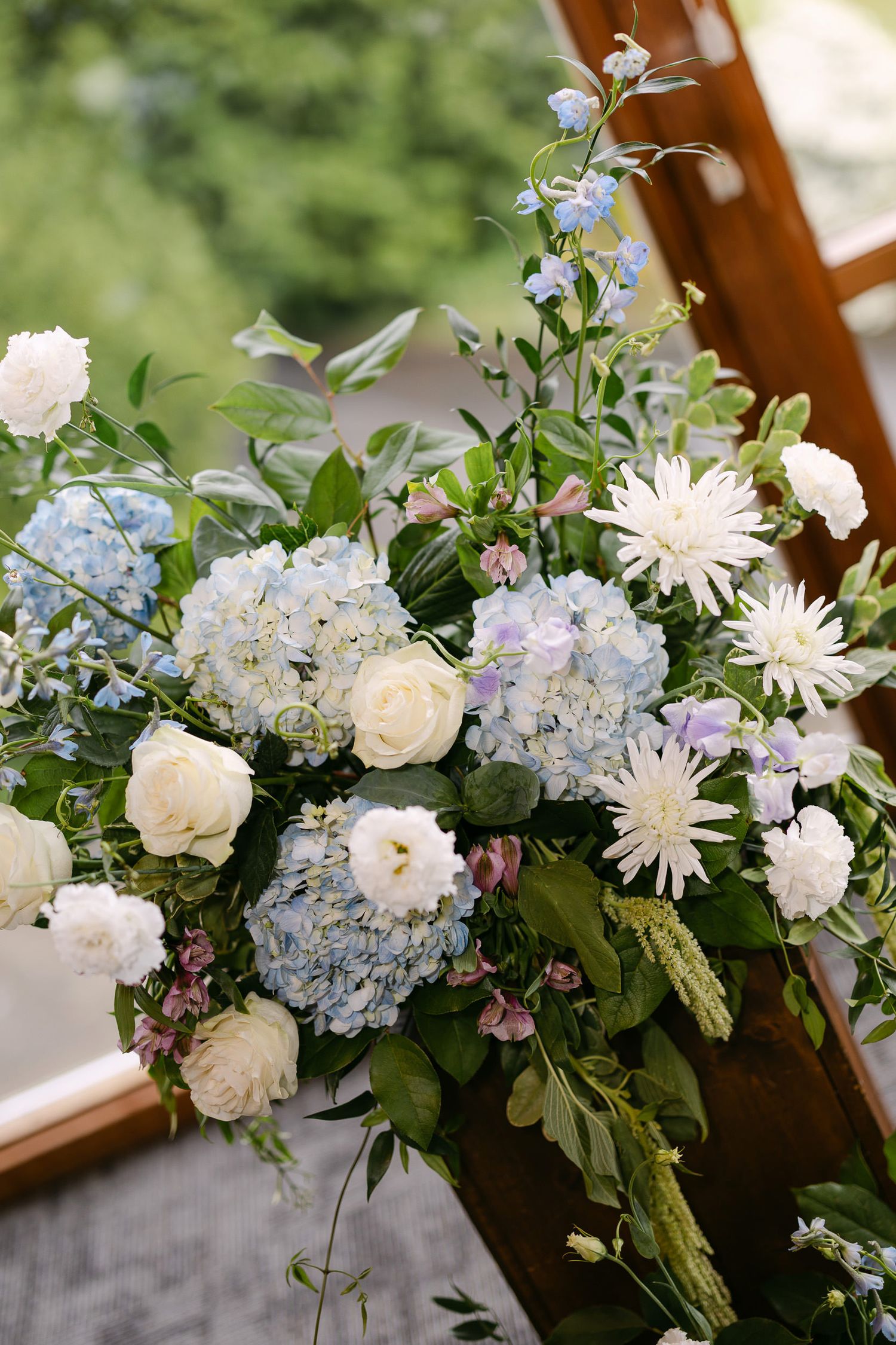 Elegant wedding floral arrangement featuring blue hydrangeas, white roses, and chrysanthemums with lush greenery.