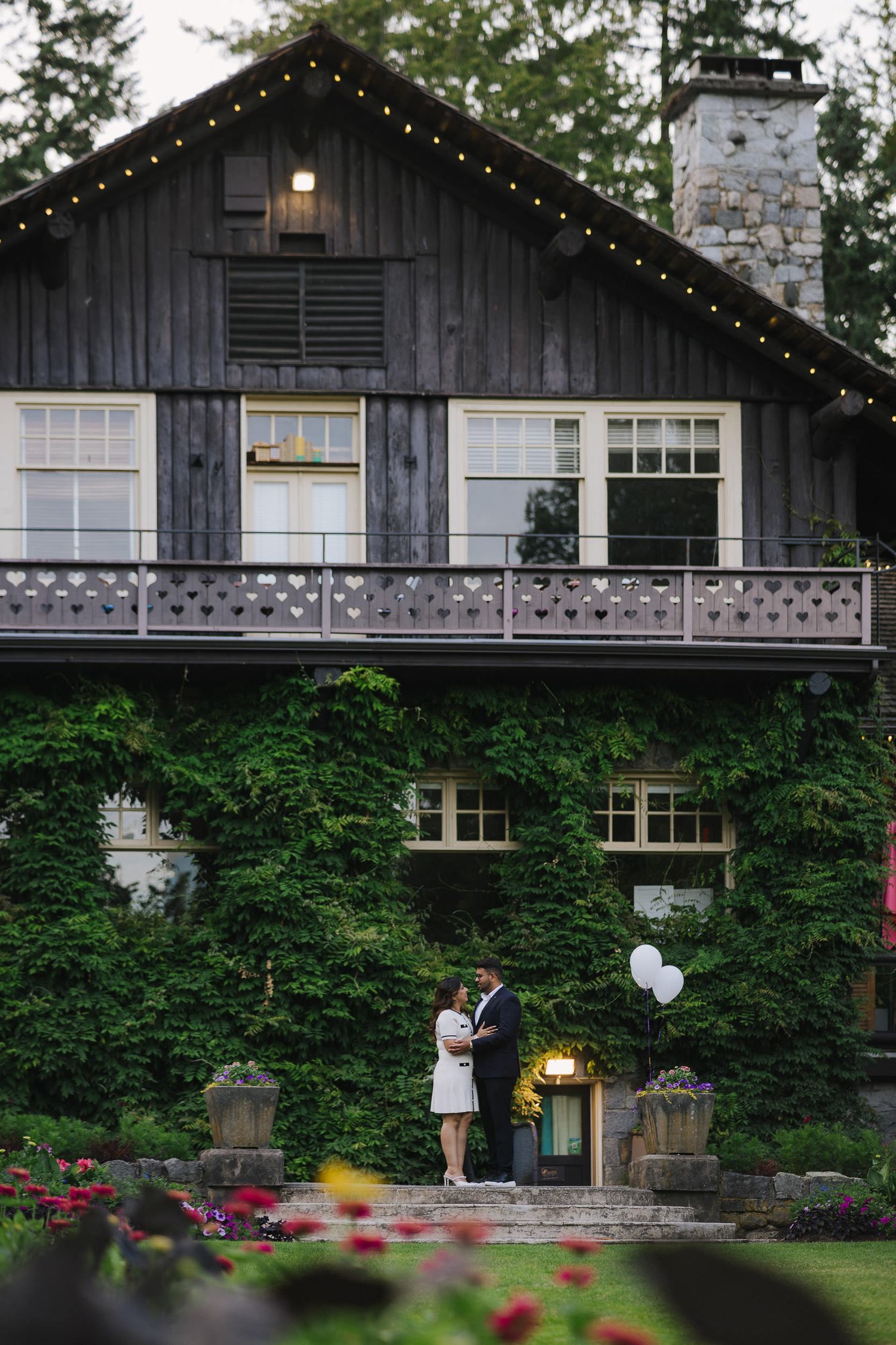 A rustic wooden lodge with stone accents and string lights surrounded by lush greenery.