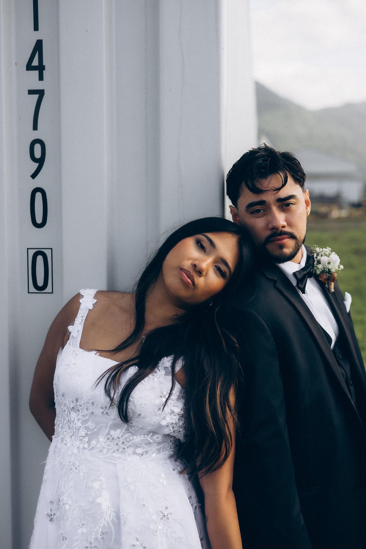 Romantic wedding couple poses intimately against white pillars in a modern architectural setting.