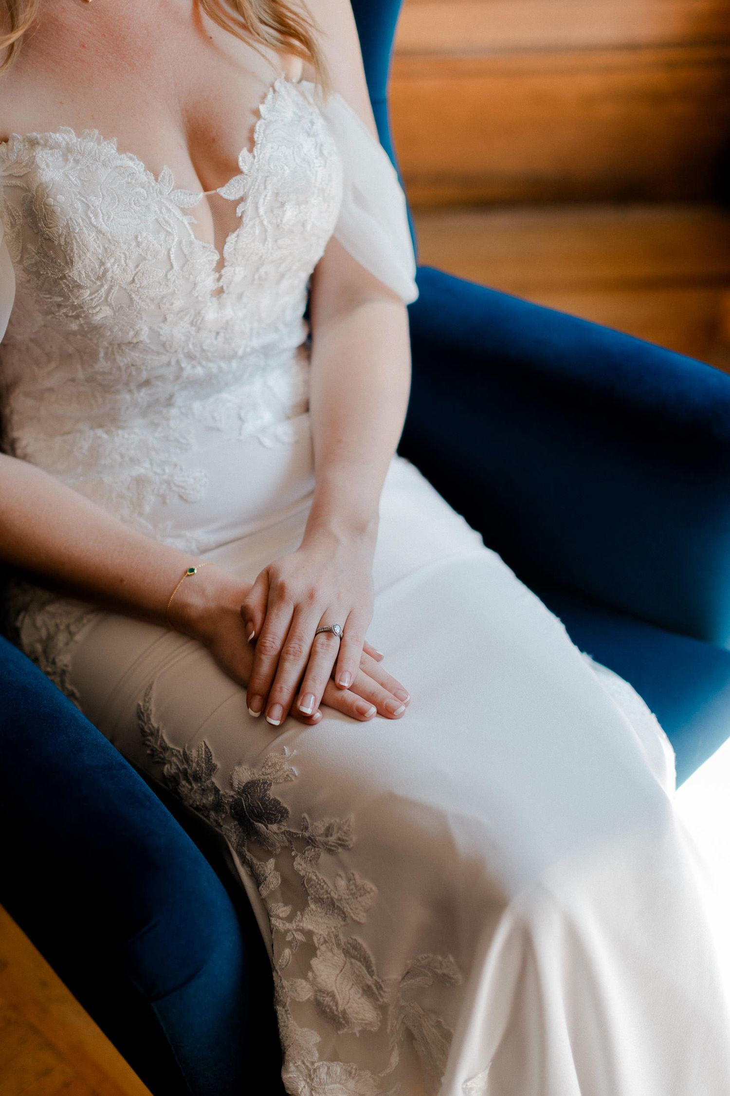 Close-up details of a white lace wedding dress with delicate floral embroidery on a navy blue chair.