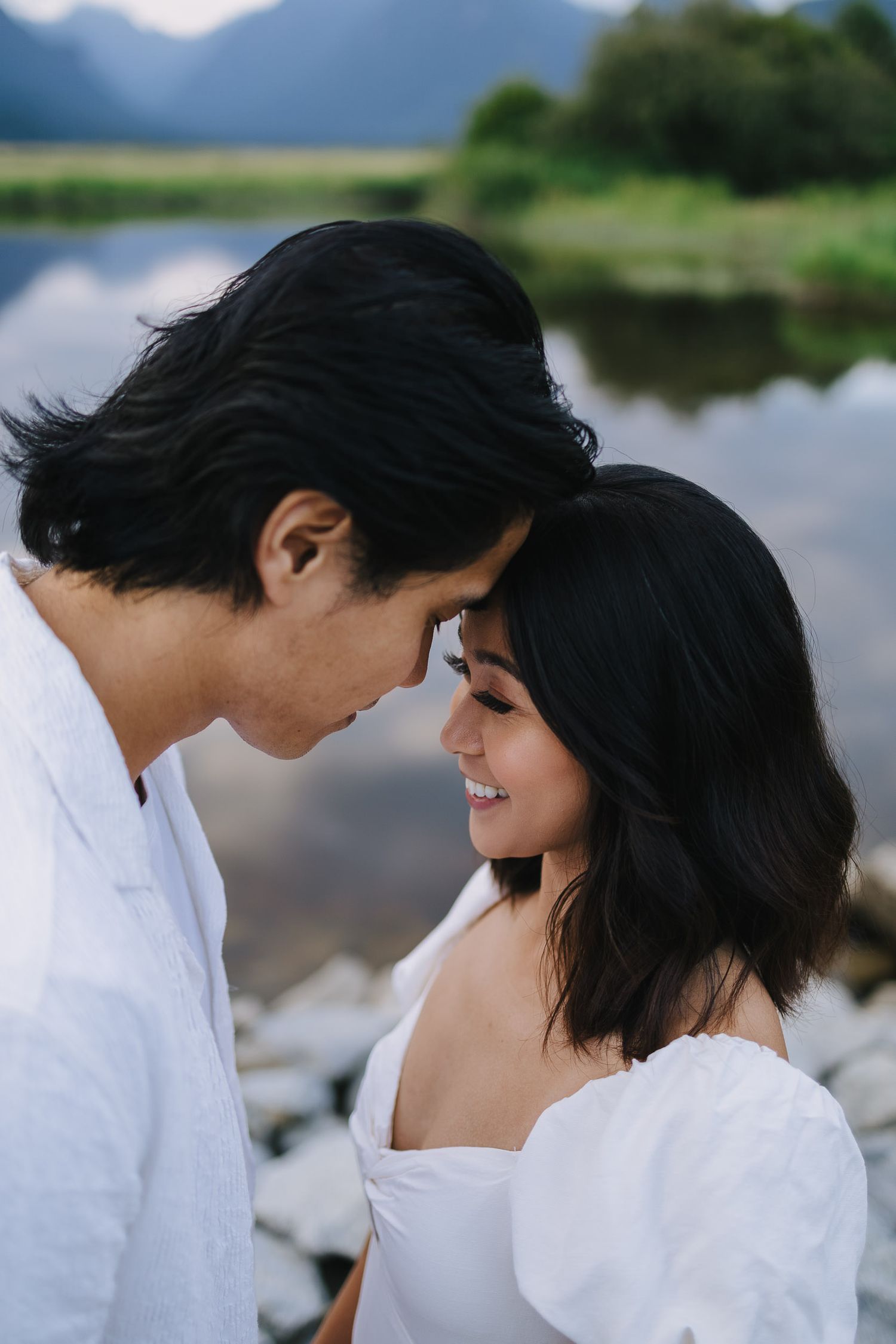 A romantic couple in white clothing share intimate moments by a serene mountain lake.